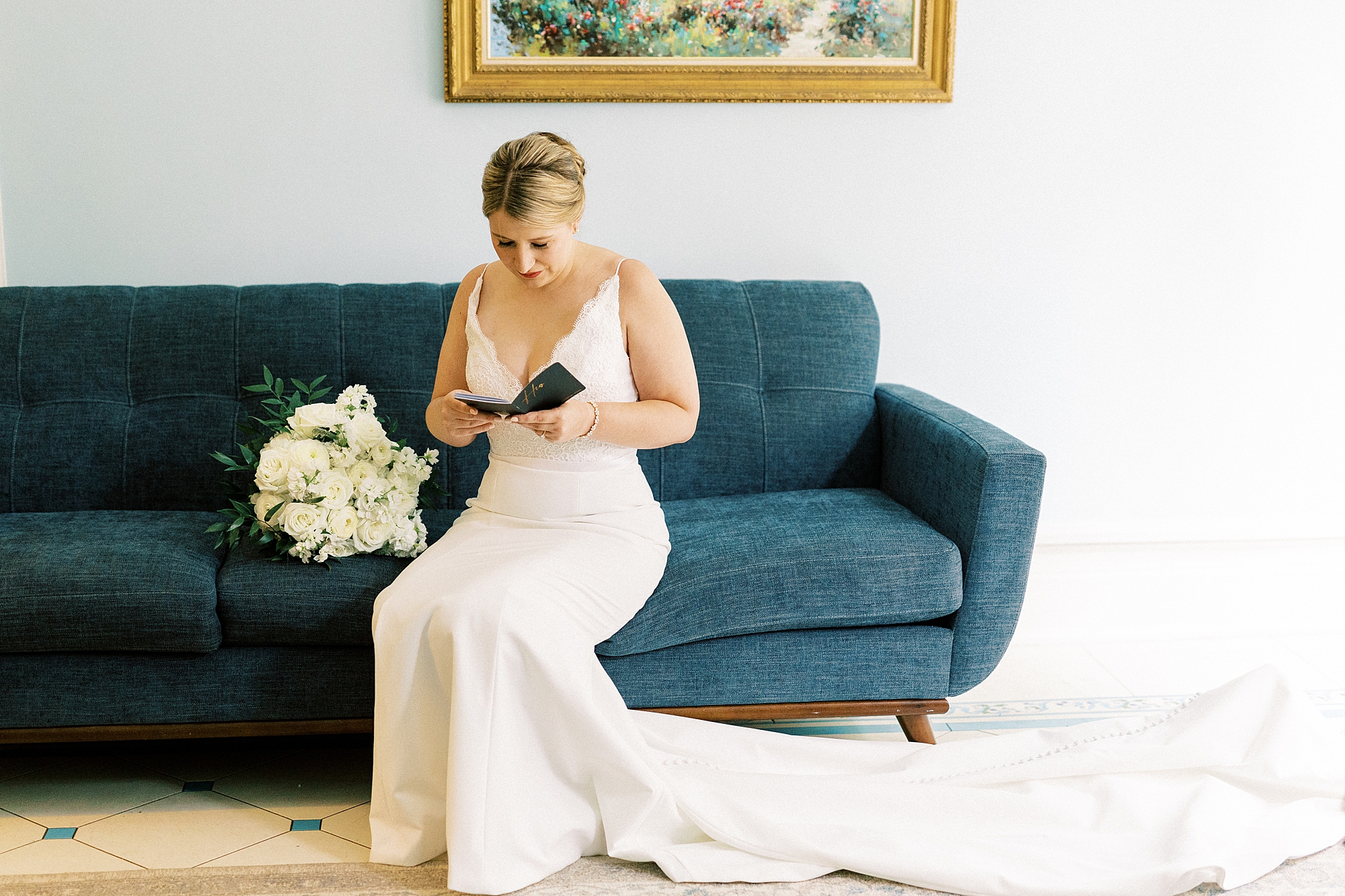 bride looks at vow booklet on sofa in suite at the Morehead Inn