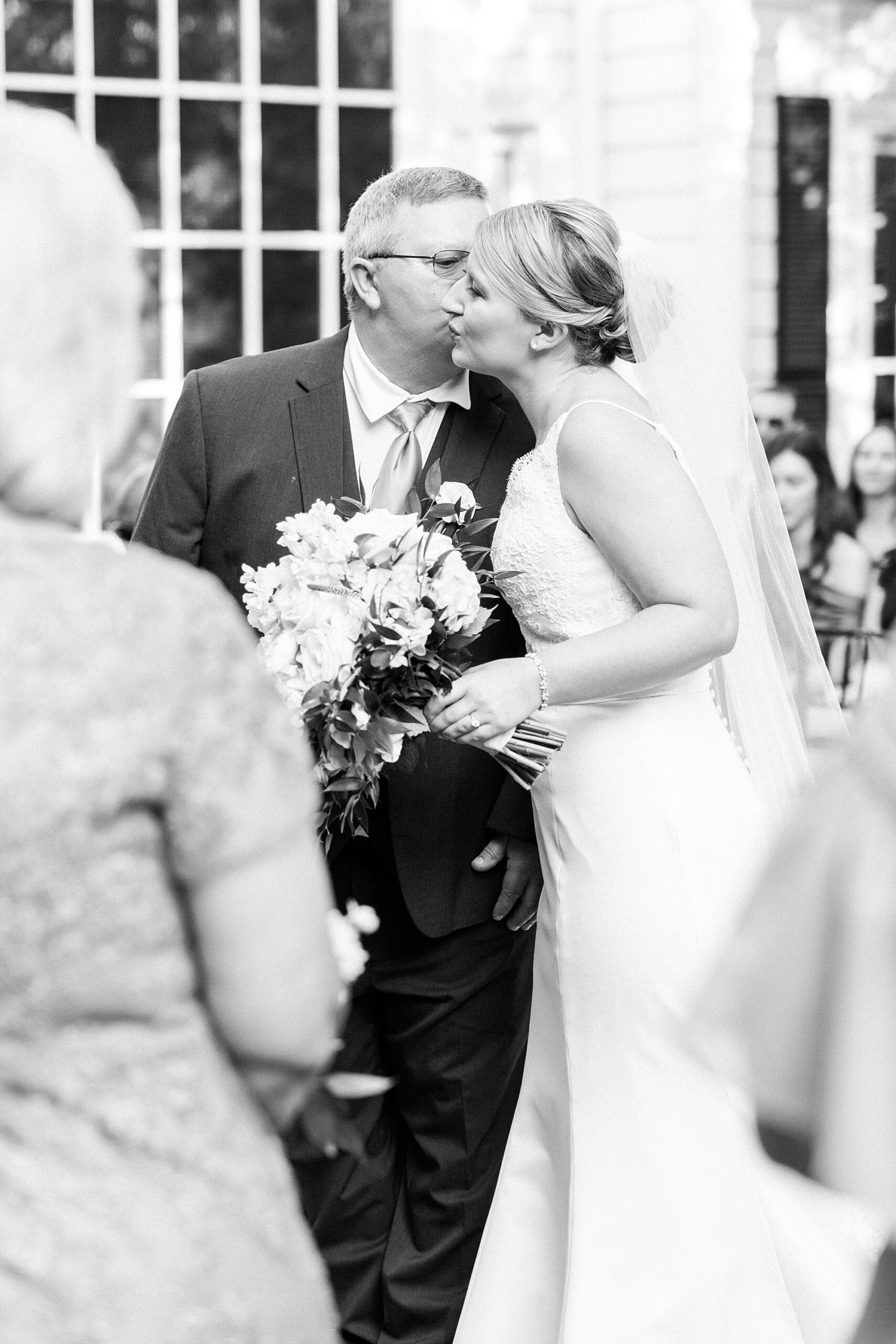 father leans to kiss bride on the cheek during wedding ceremony at the Morehead Inn