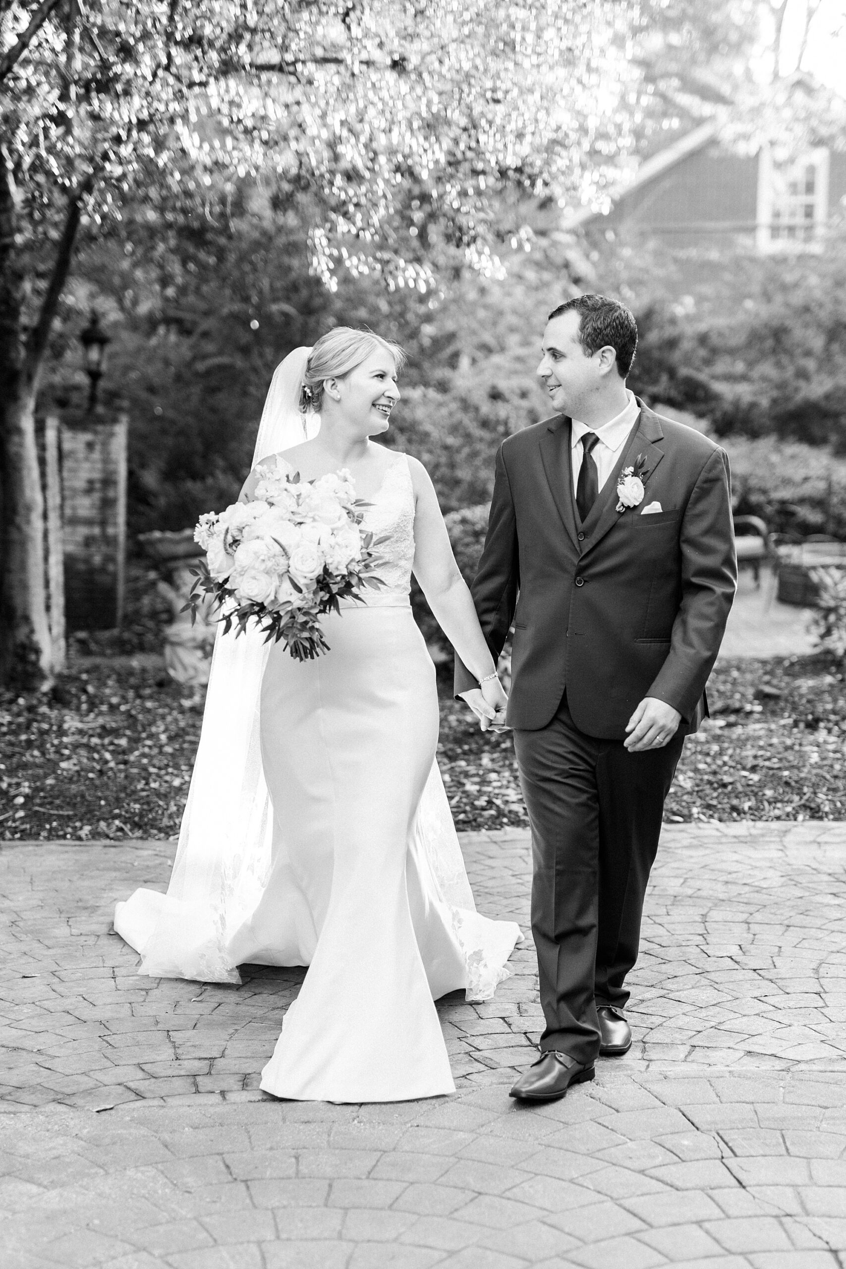 bride and groom hold hands walking across patio at the Morehead Inn