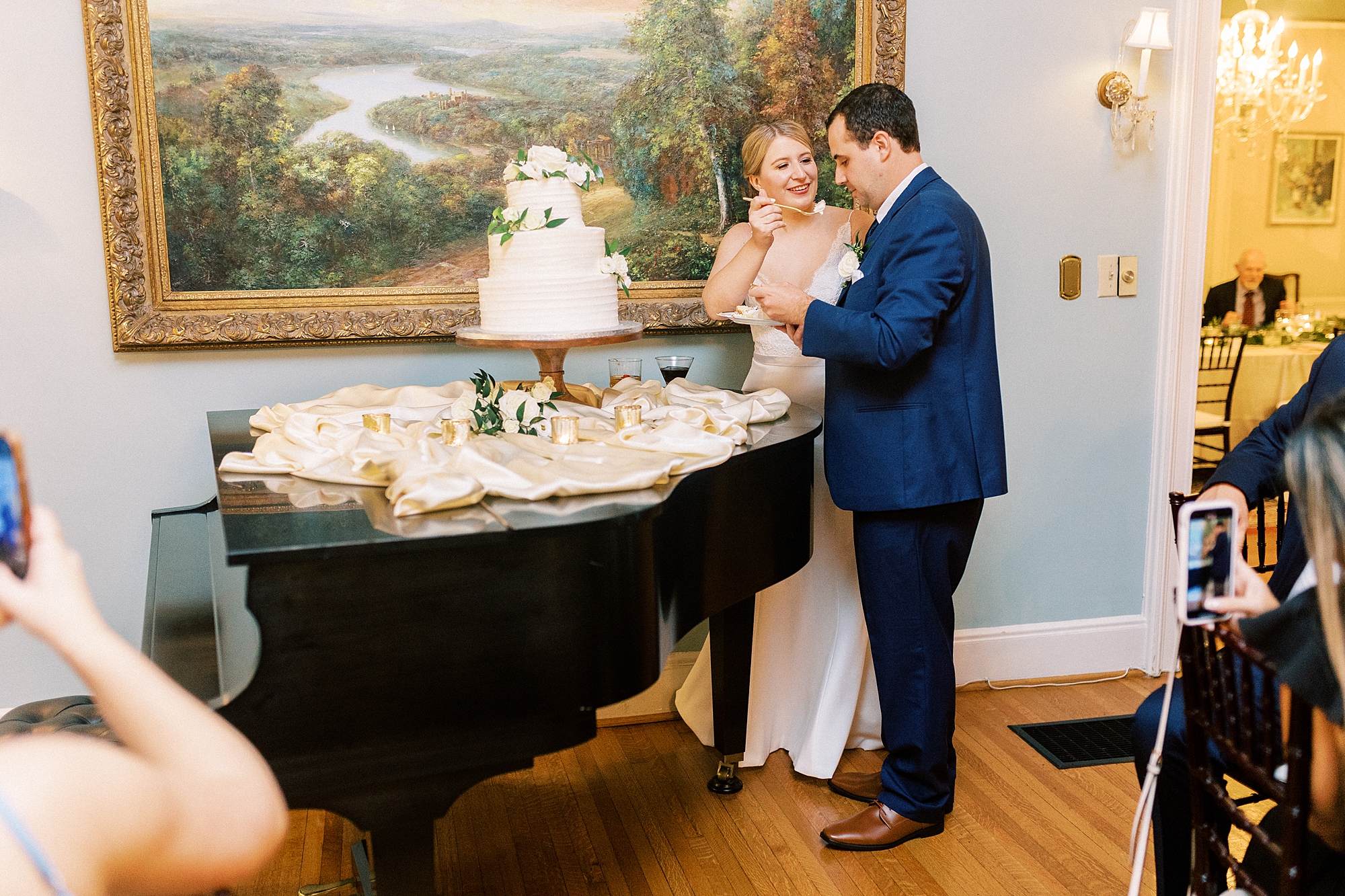 newlyweds cut wedding cake on top of piano at the Morehead Inn