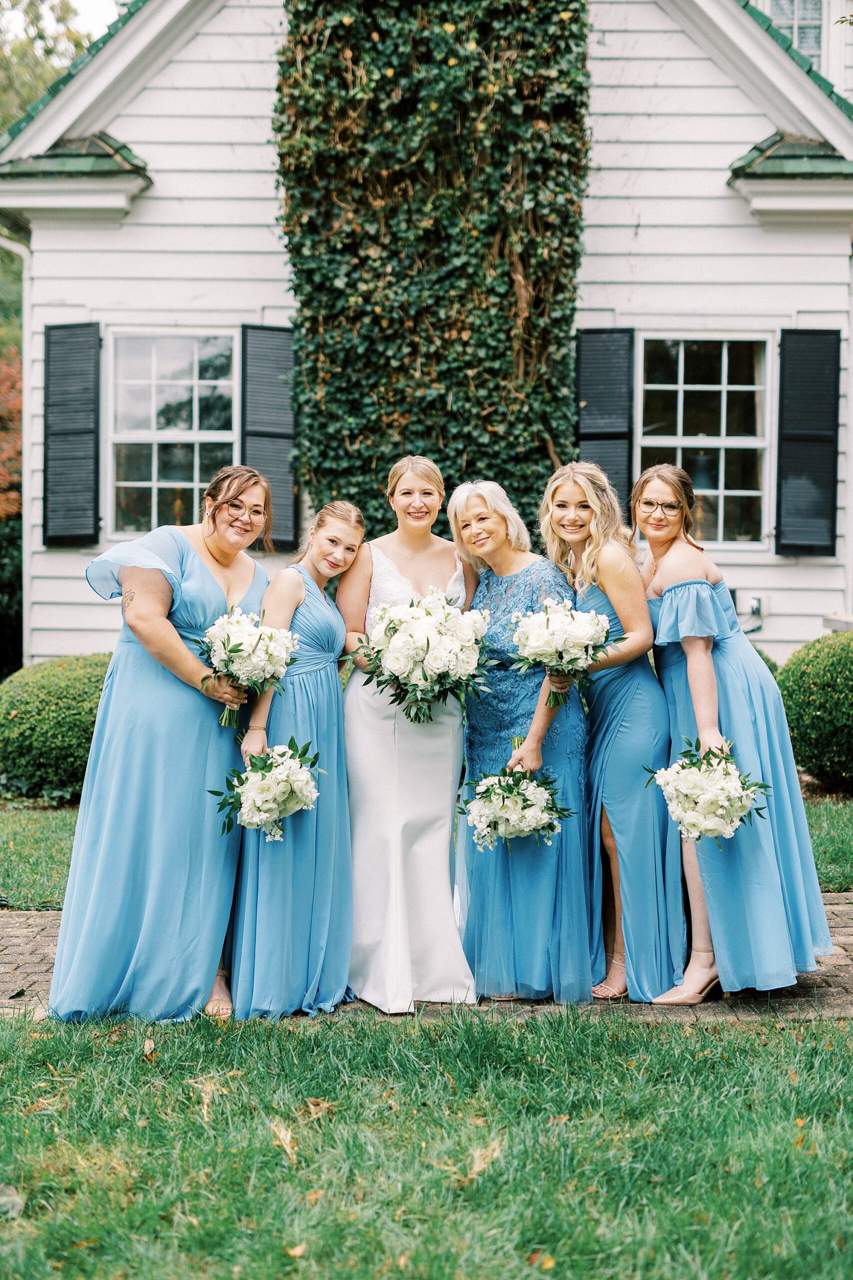 bride poses with bridesmaids in light blue gowns outside the Morehead Inn