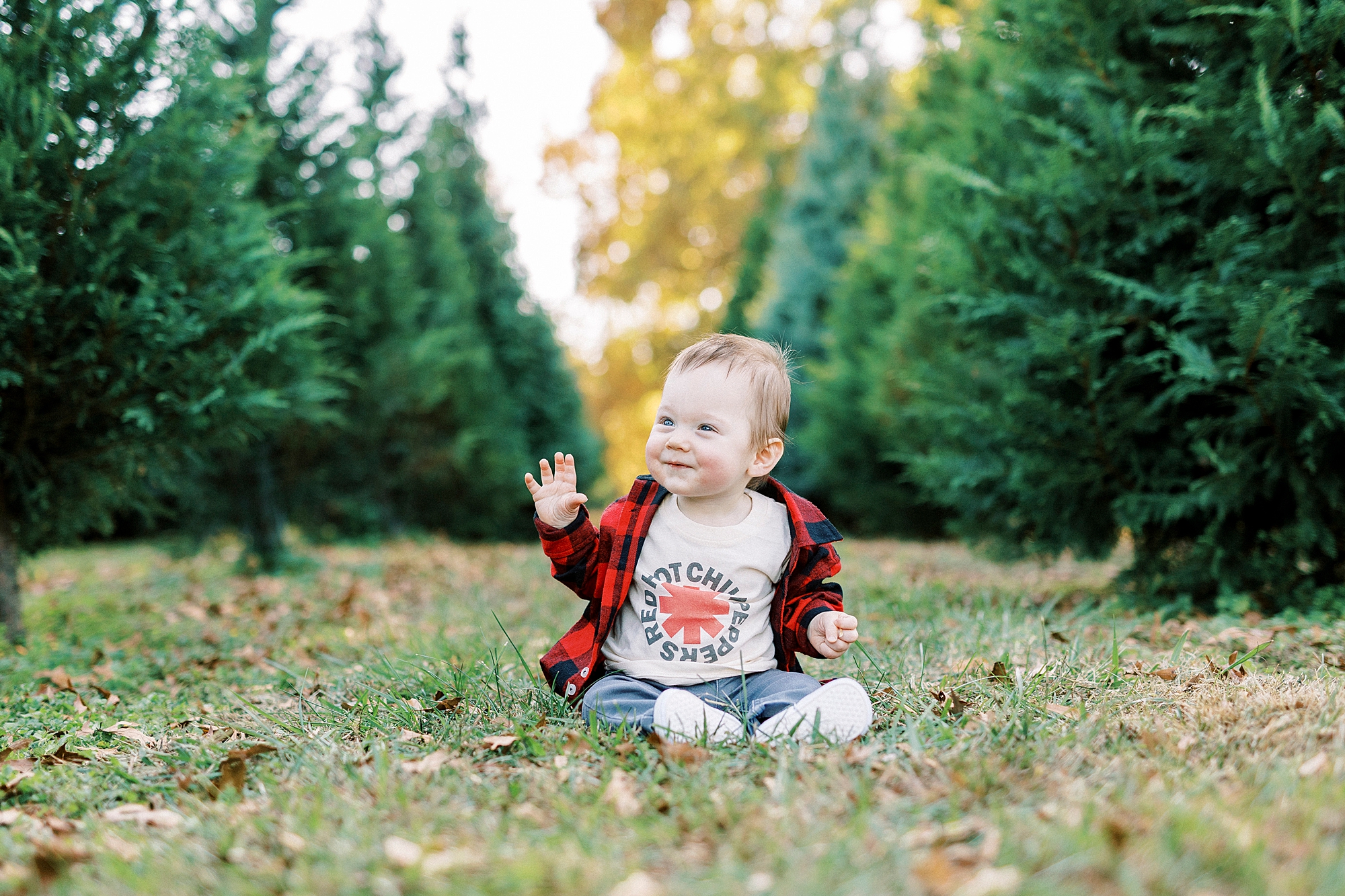 baby sits between trees waving during Almond Christmas Tree Farm mini sessions 