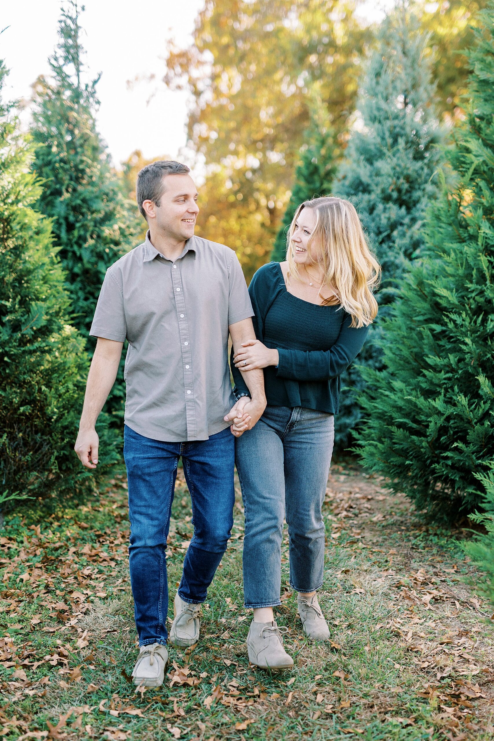 engaged couple bumps hips between trees at Almond Christmas Tree Farm
