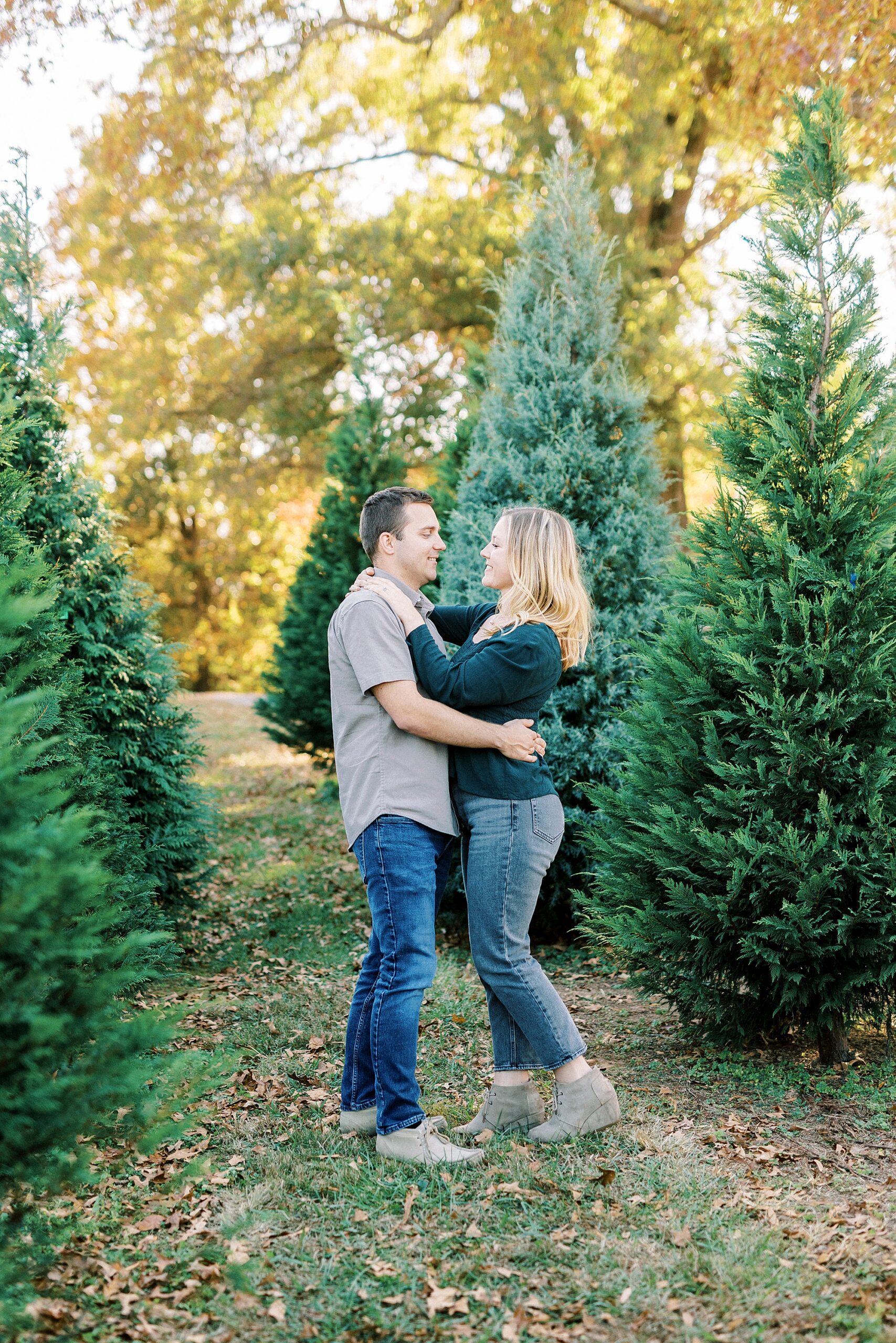 man and woman hug facing each other between trees at Almond Christmas Tree Farm