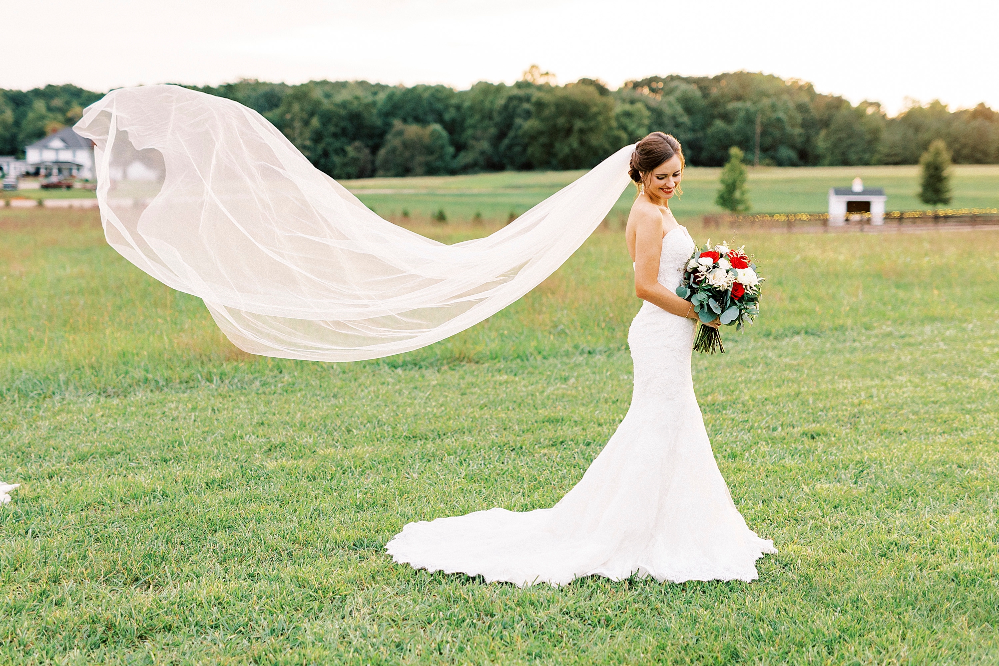 bride looks down at bouquet while veil floats behind her at Chickadee Hill Farms