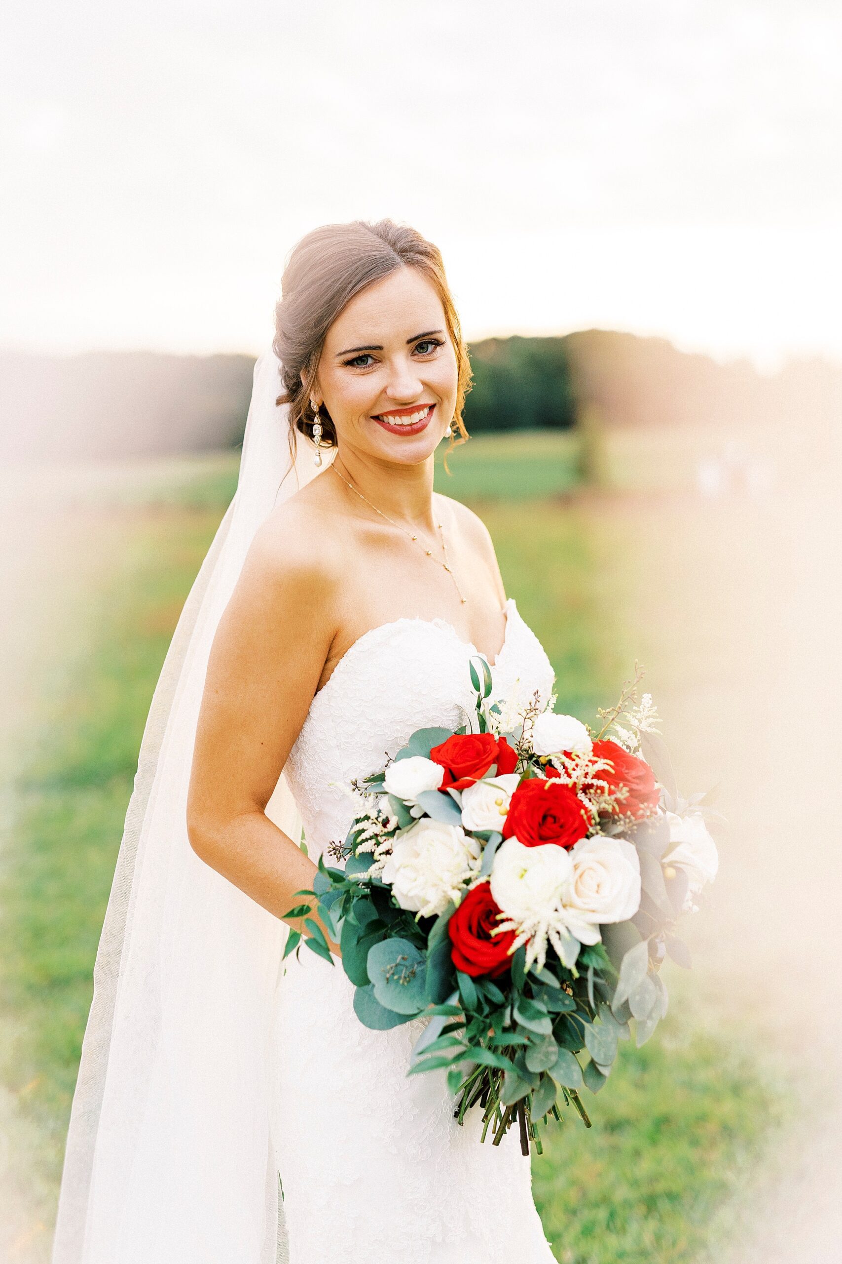 bride stands holding bouquet of red and white flowers 