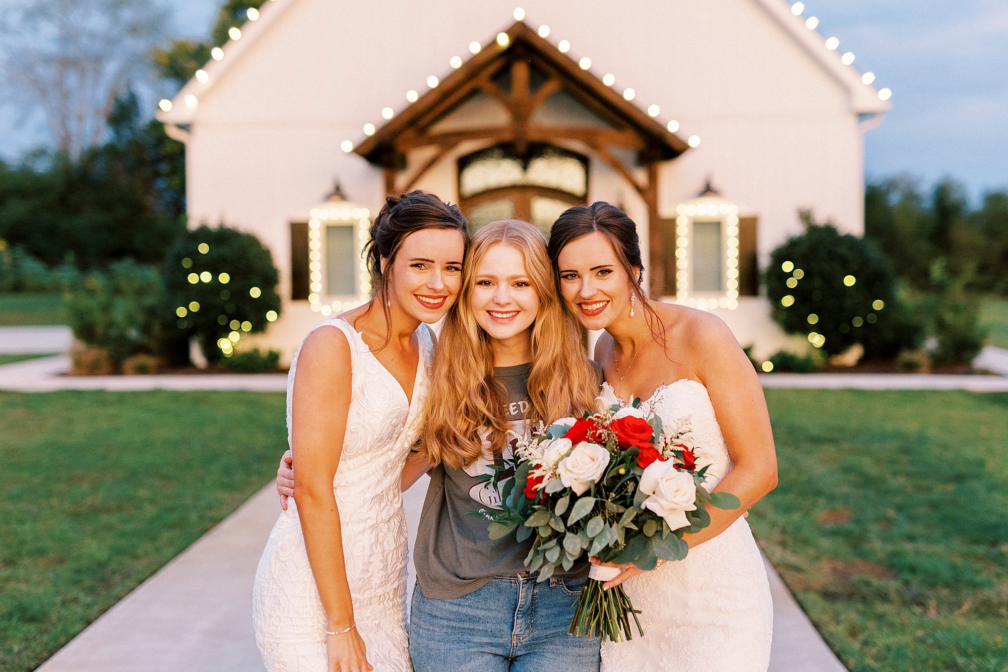 bride poses with sisters in front of chapel at Chickadee Hill Farms