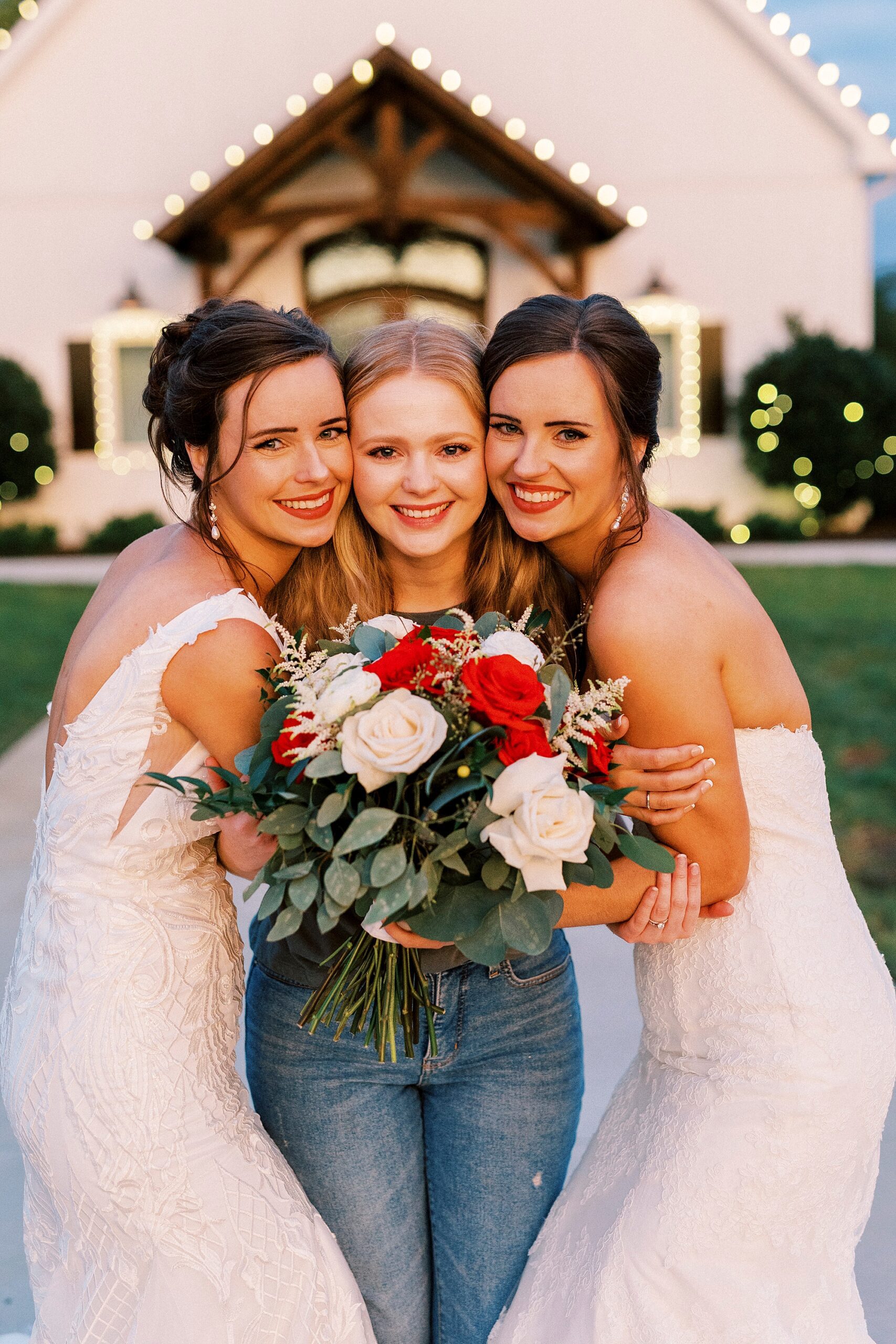 bride and sisters hug in front of chapel at Chickadee Hill Farms