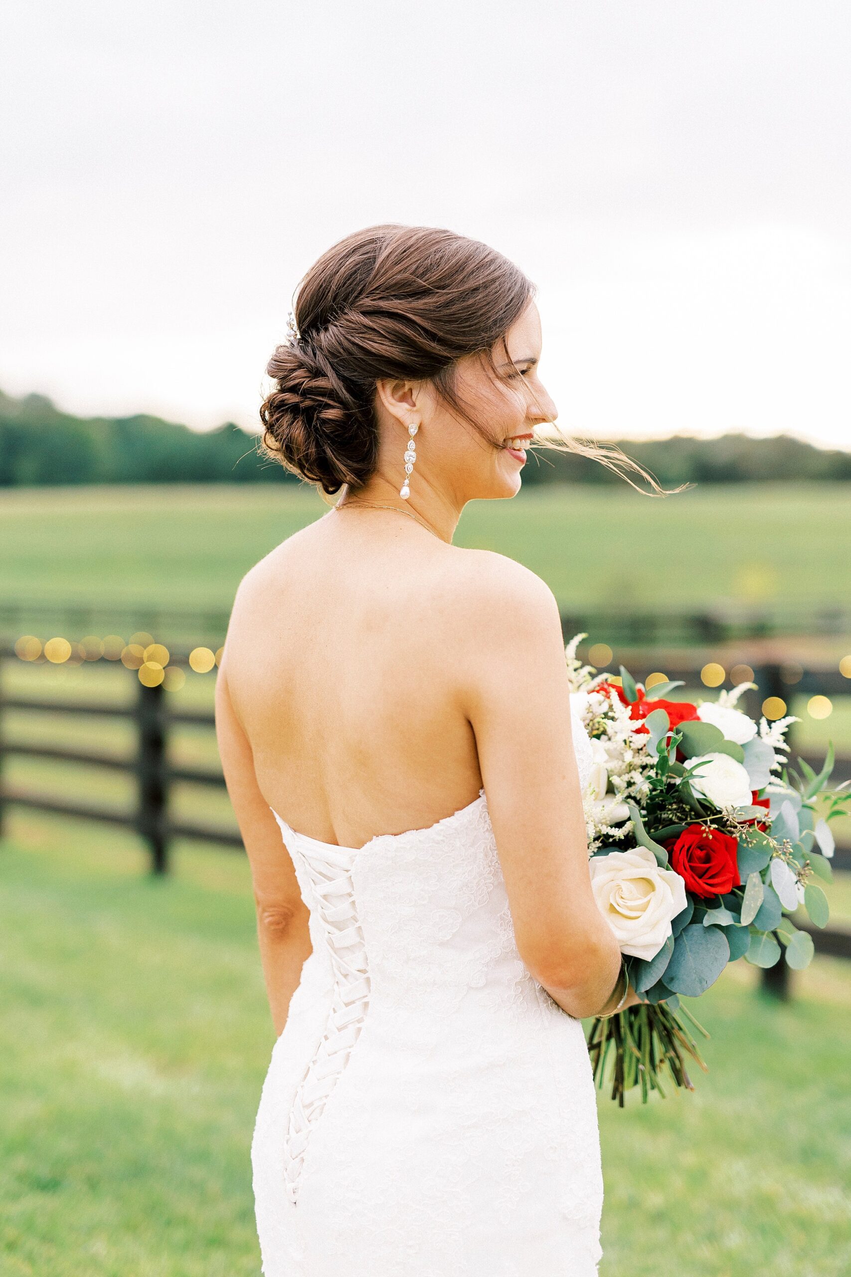 bride looks over shoulder holding red and white flowers at Chickadee Hill Farms