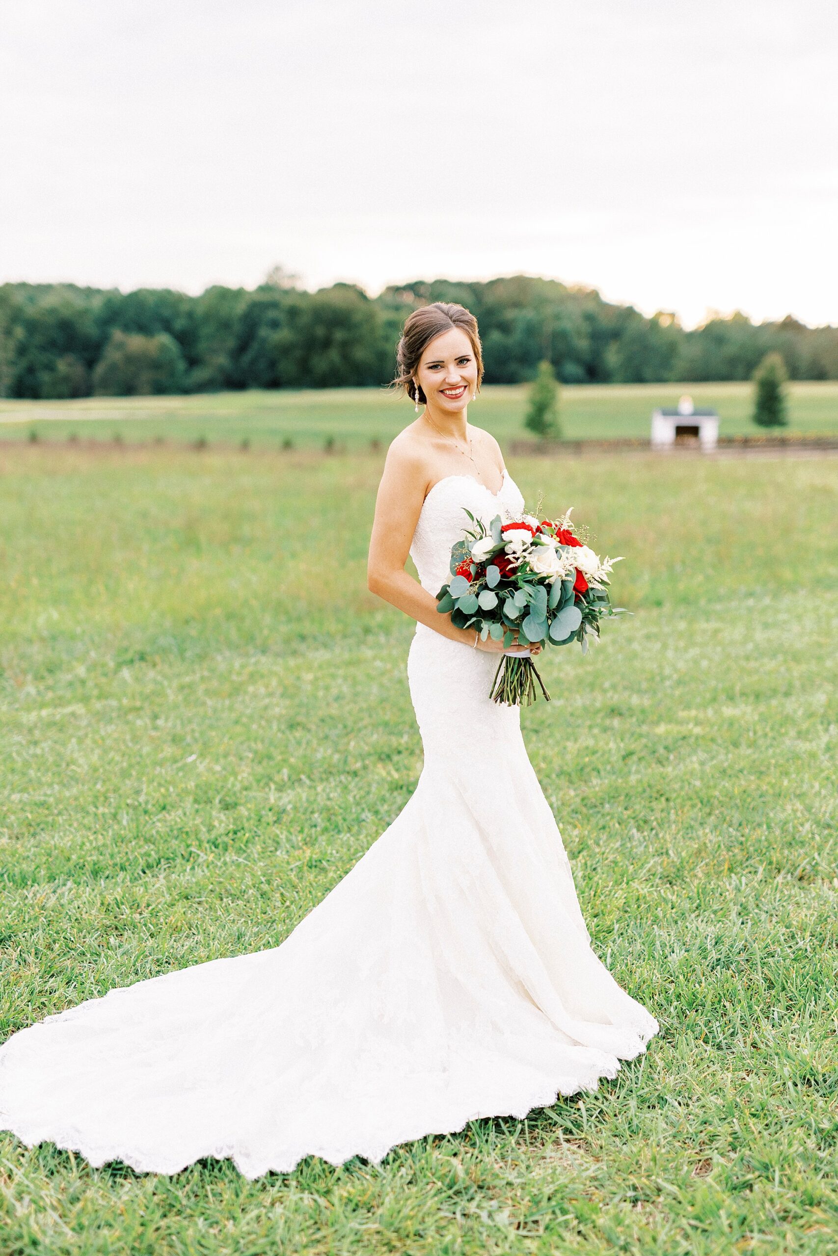 bride poses holding bouquet of white and red flowers at Chickadee Hill Farms