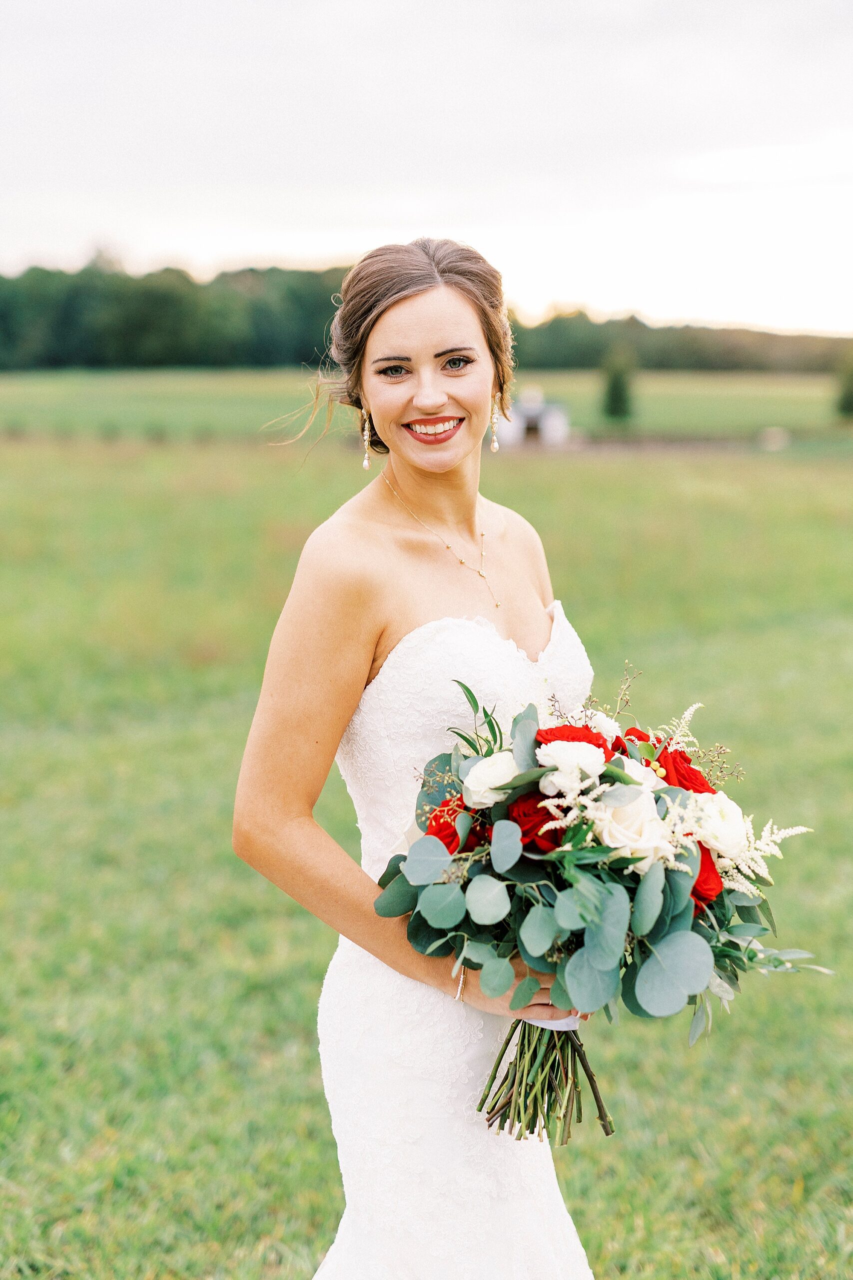 bride in strapless wedding gown holds bouquet of white and red flowers 
