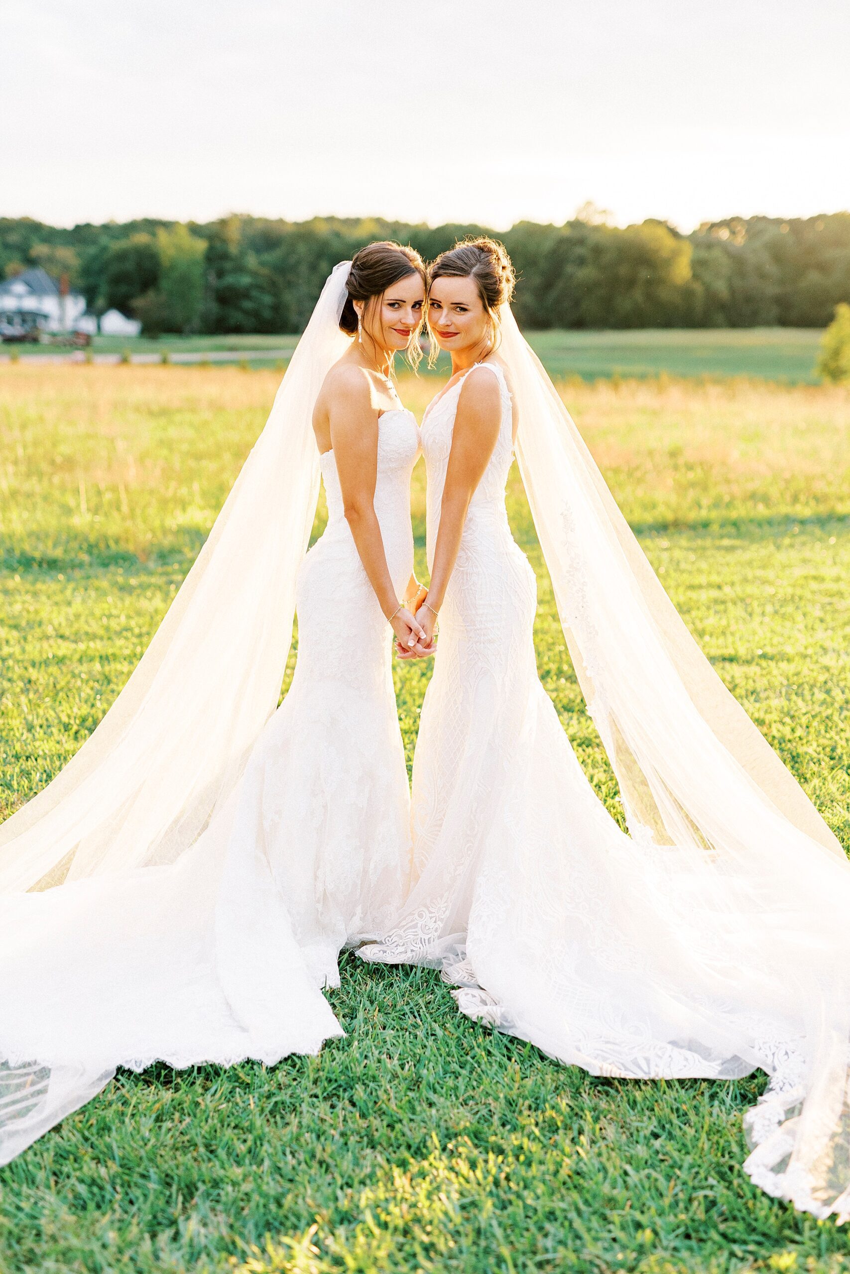 bride and sister hold hands leaning together in front of sunset at Chickadee Hill Farms