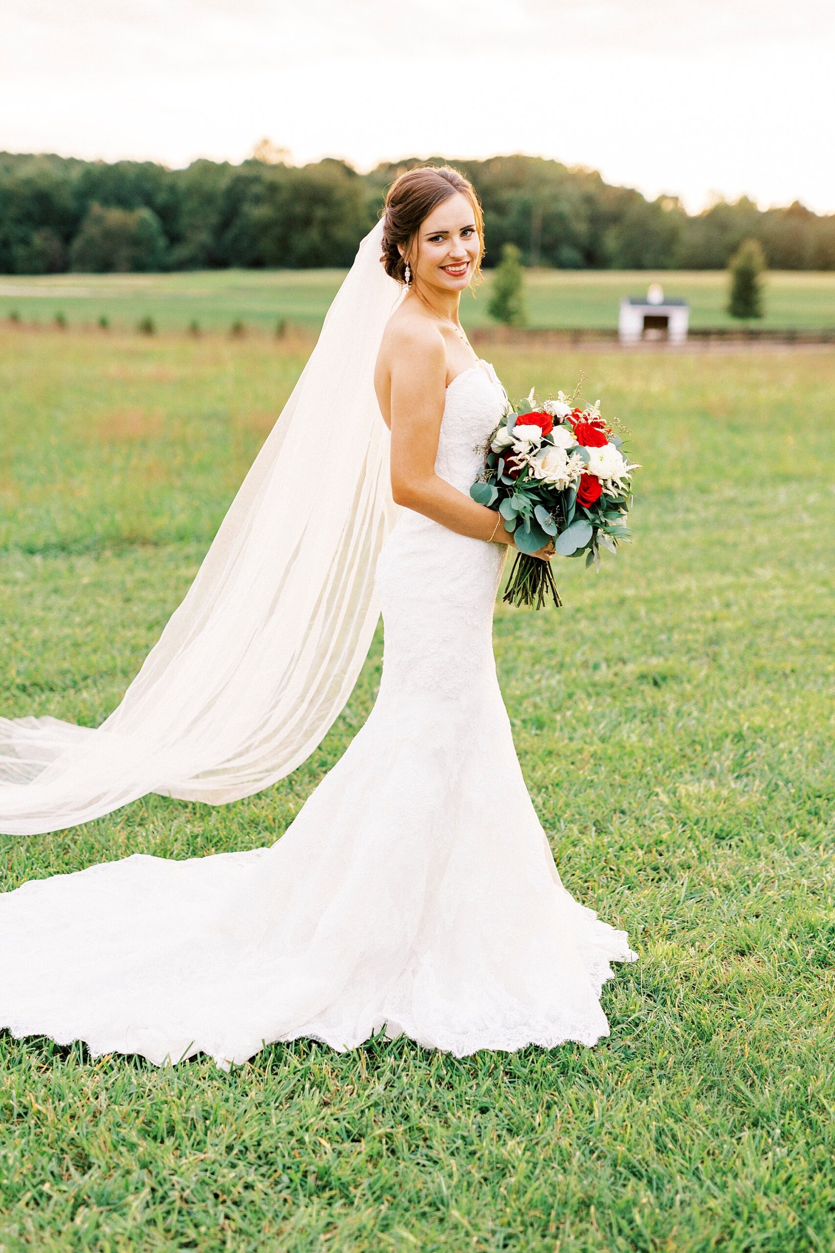 bride walks across lawn in wedding gown with red and white flowers