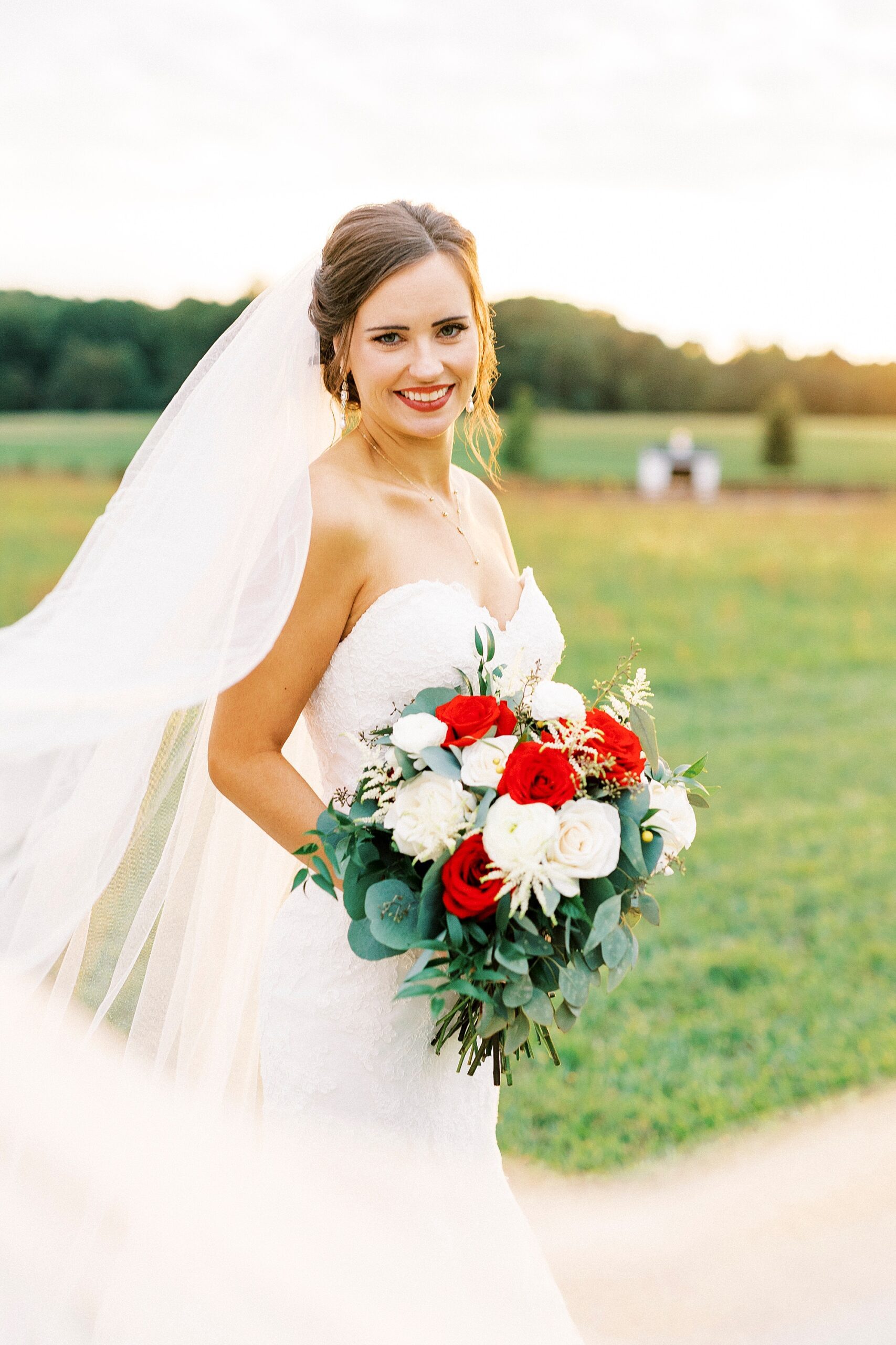 bride stands holding bouquet of red and white flowers at Chickadee Hill Farms