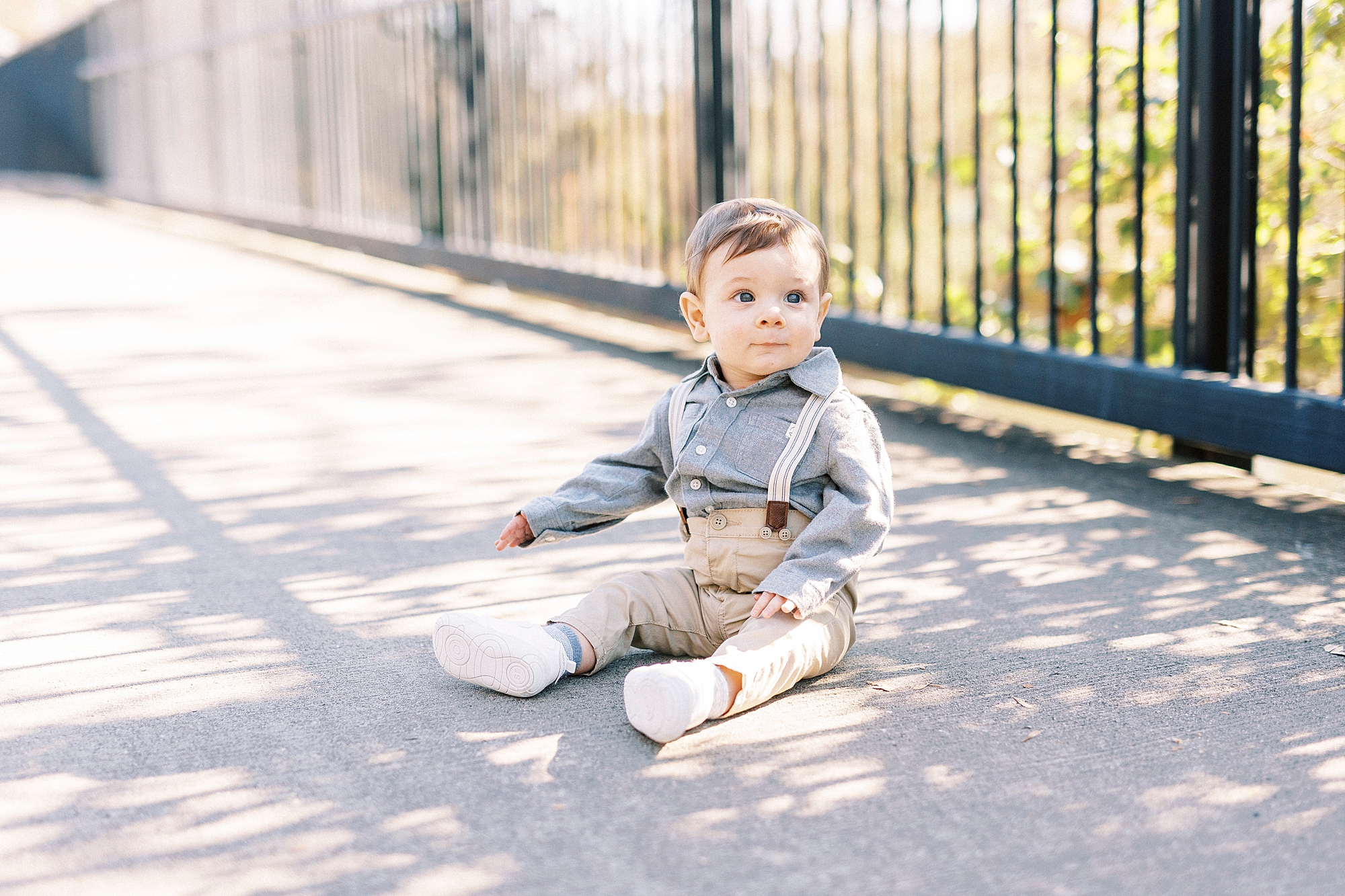 boy sits in suspenders and blue button up shirt during fall family photos