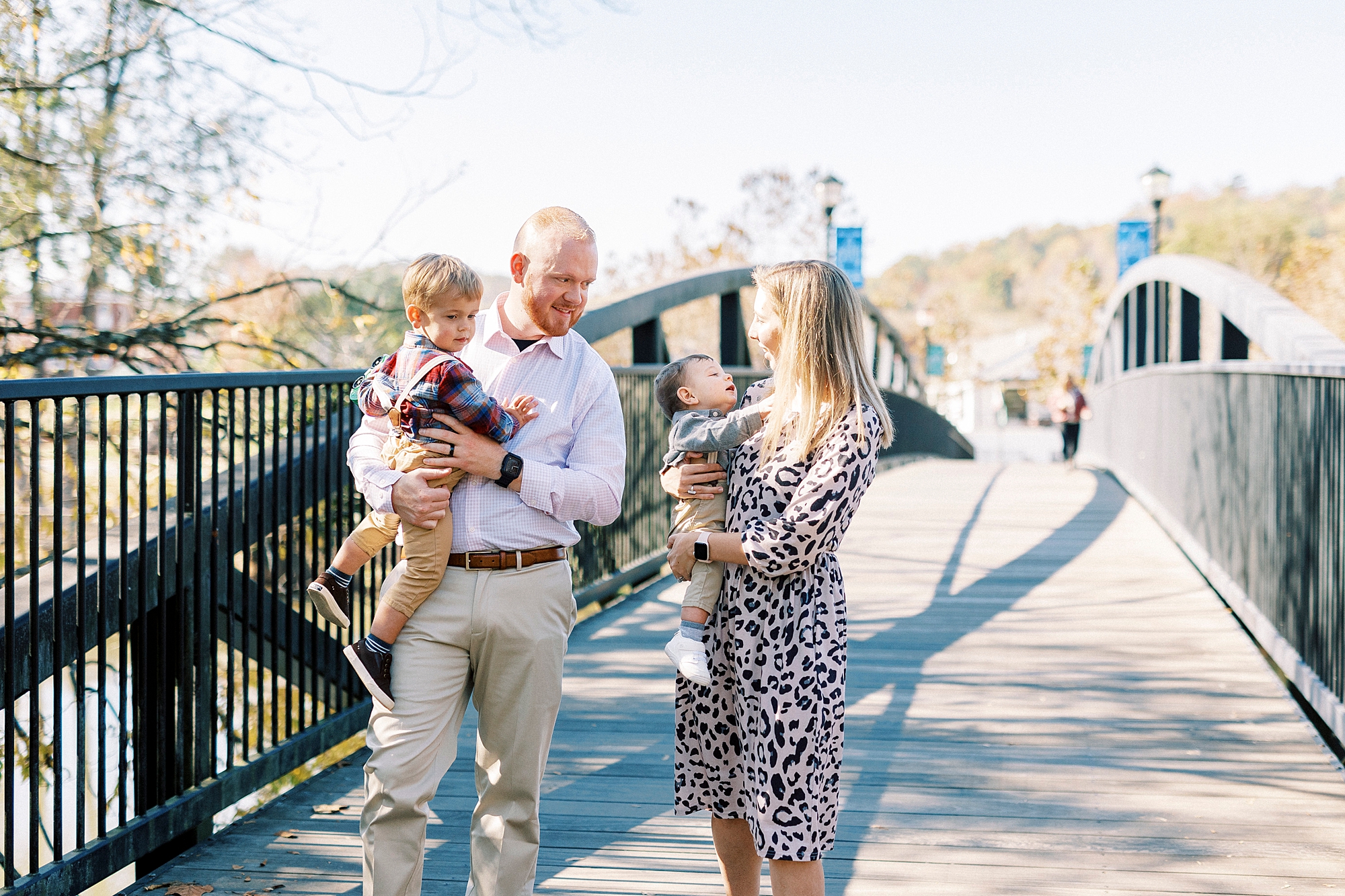 parents walk across bridge carrying sons during lifestyle fall family portraits
