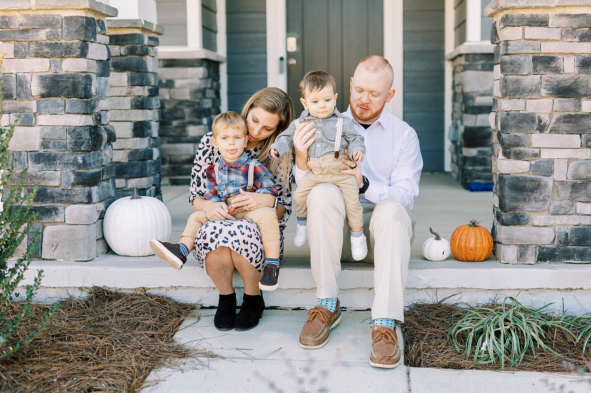 mom and dad sit on front porch holding sons on lap during lifestyle fall family portraits