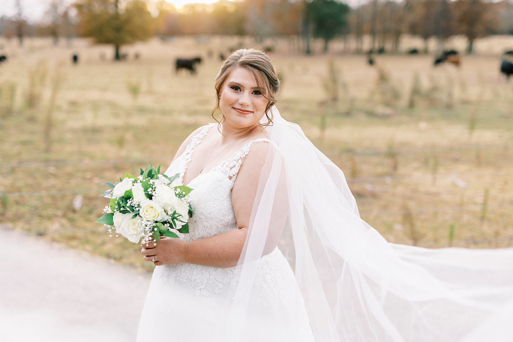 bride smiles holding bouquet of flowers with veil floating around her