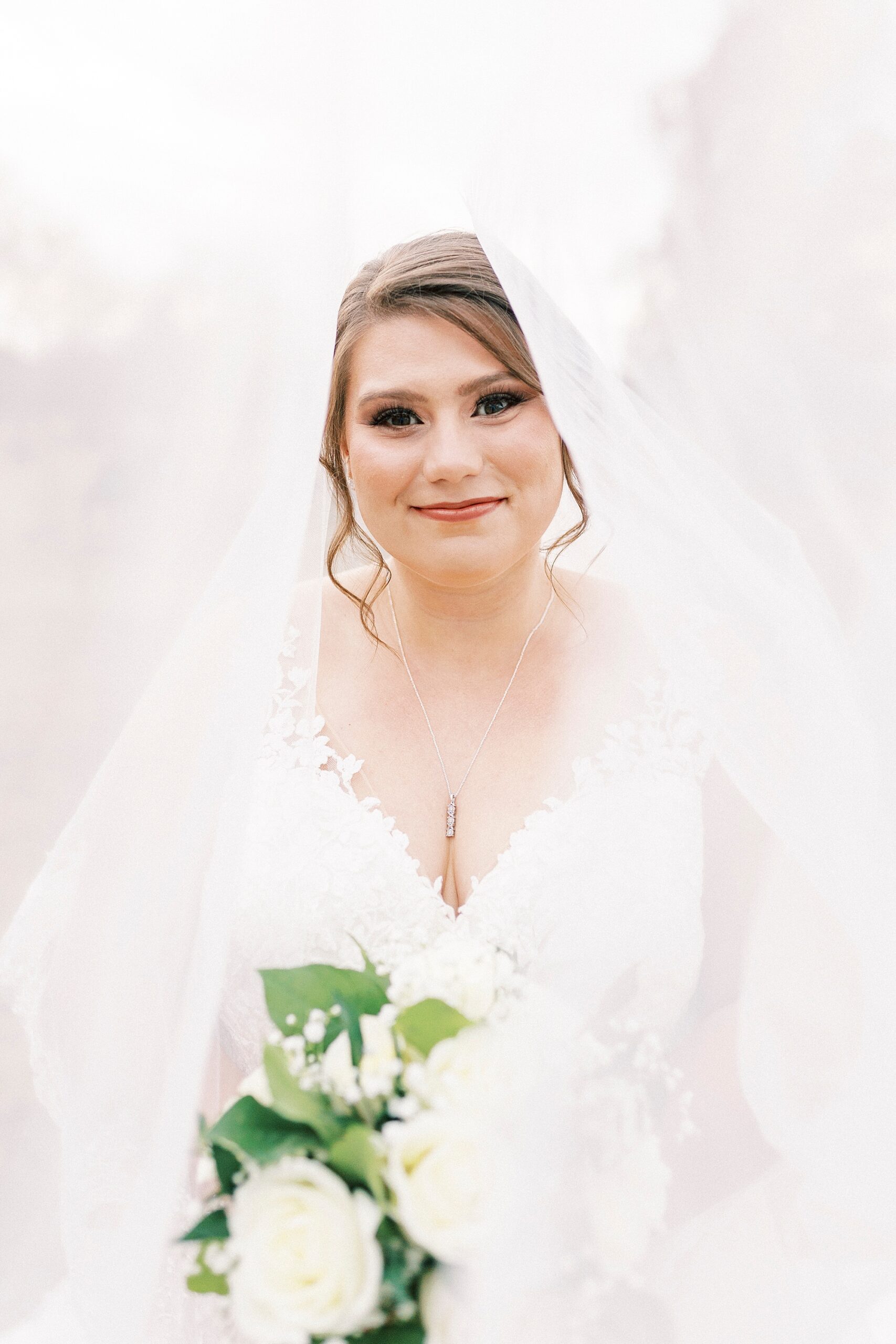 bride smiles with head tilted to left with veil over top of her 