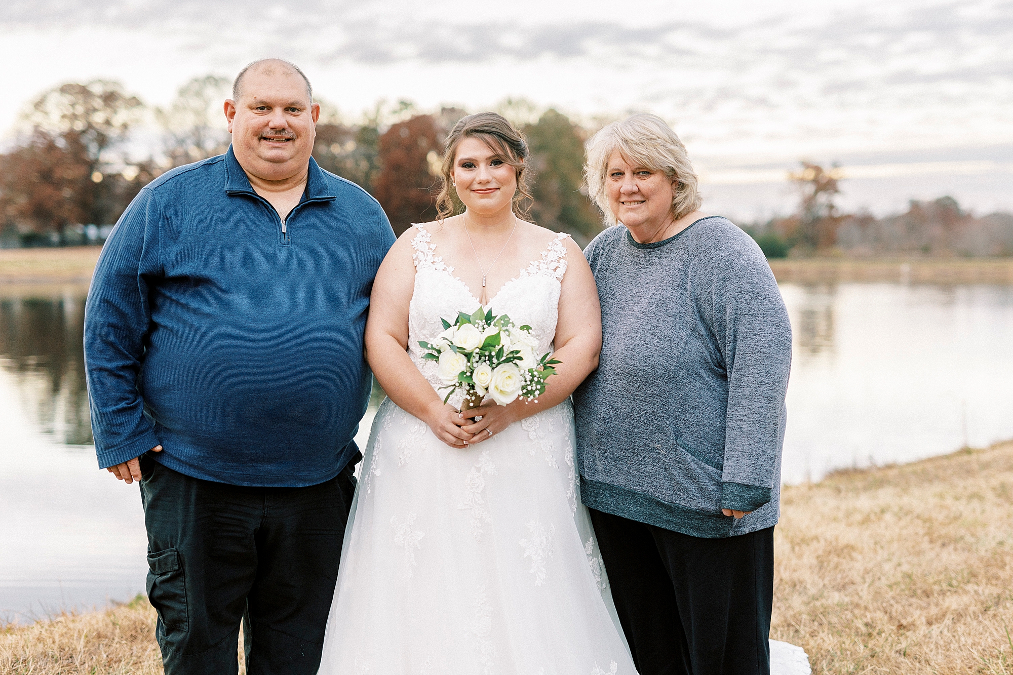 bride stands with parents near pond at the Farm at Brusharbor