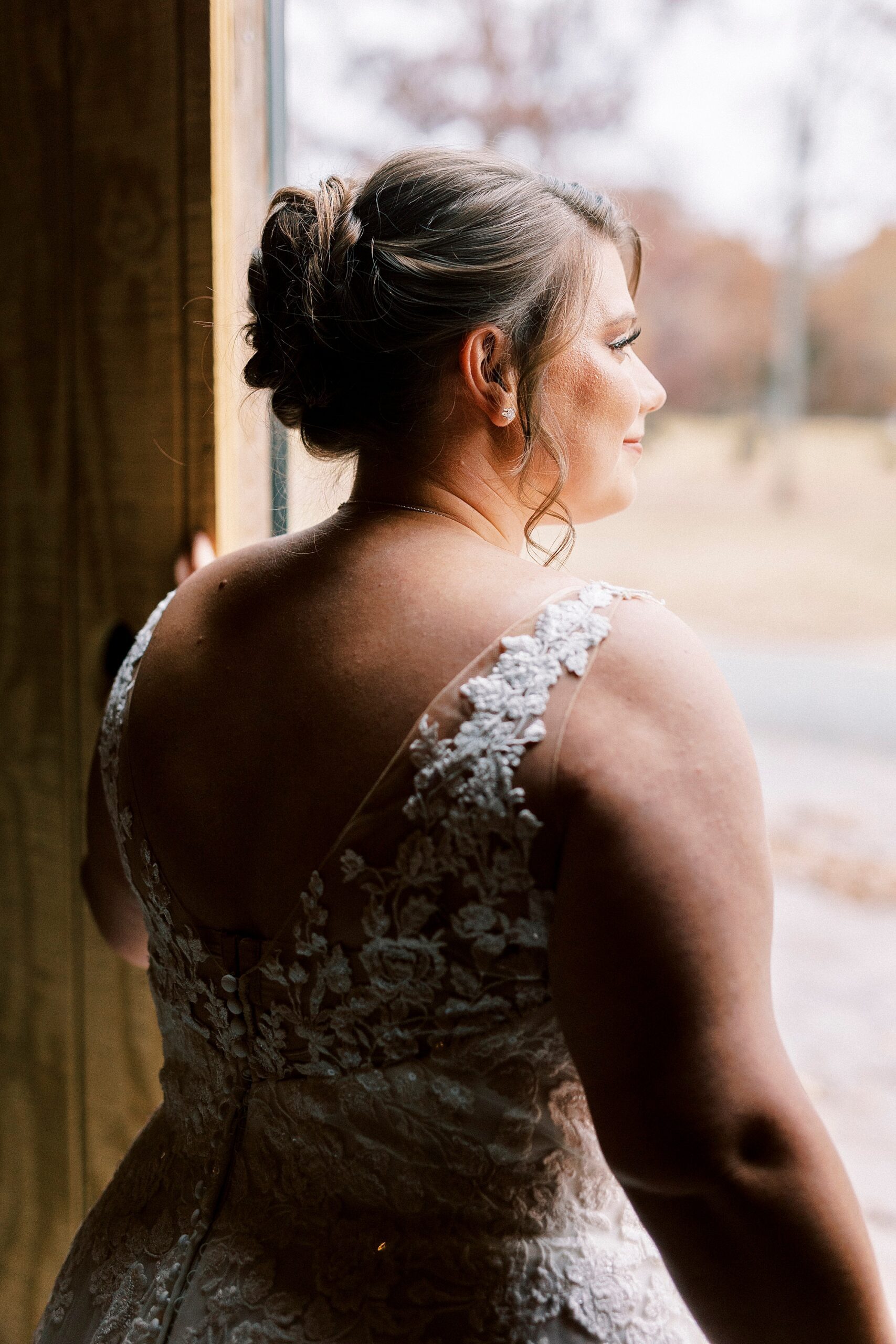 bride smiles looking out of barn door in wedding dress with lace straps 
