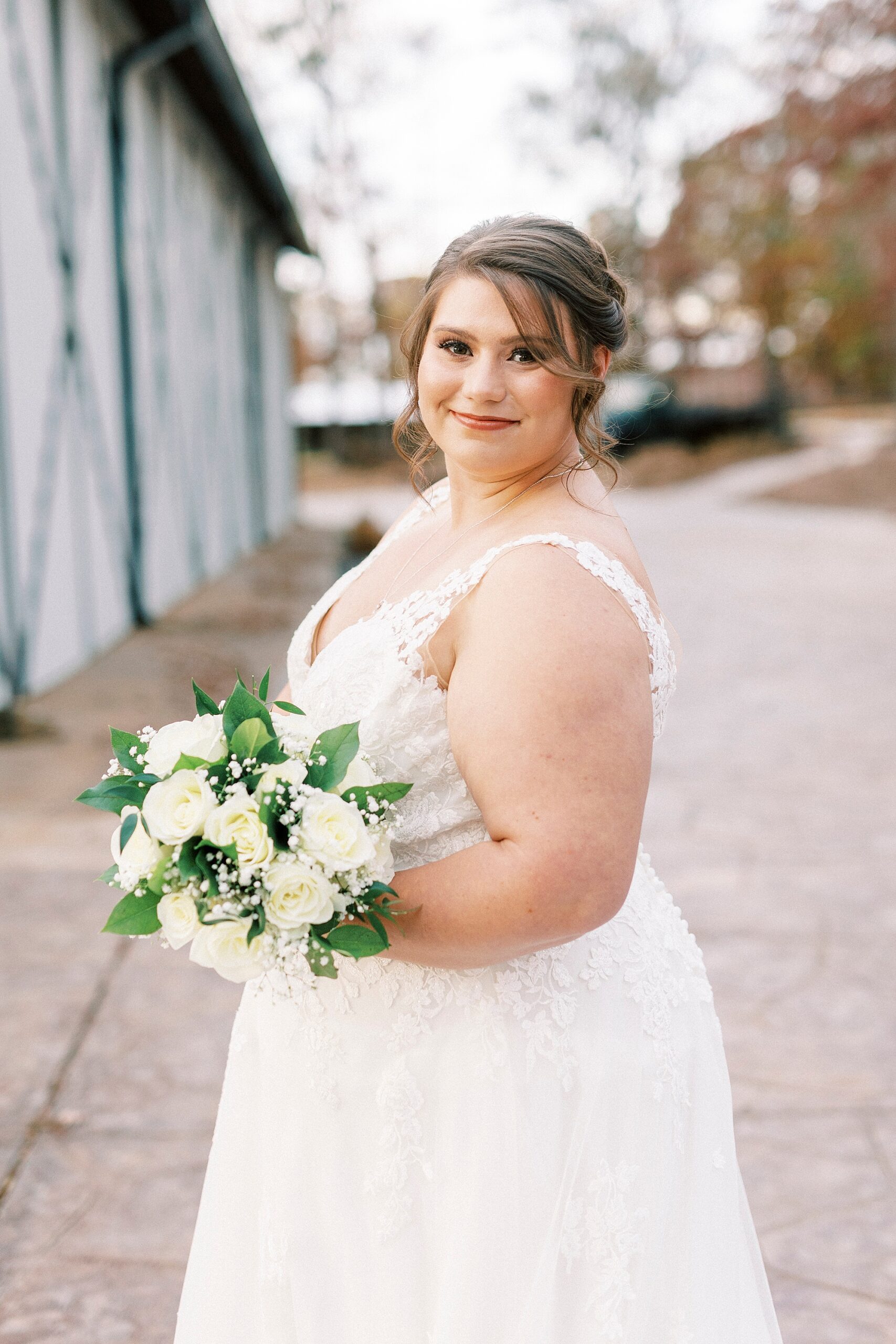 bride holds bouquet of white roses and baby's breath looking over shoulder 