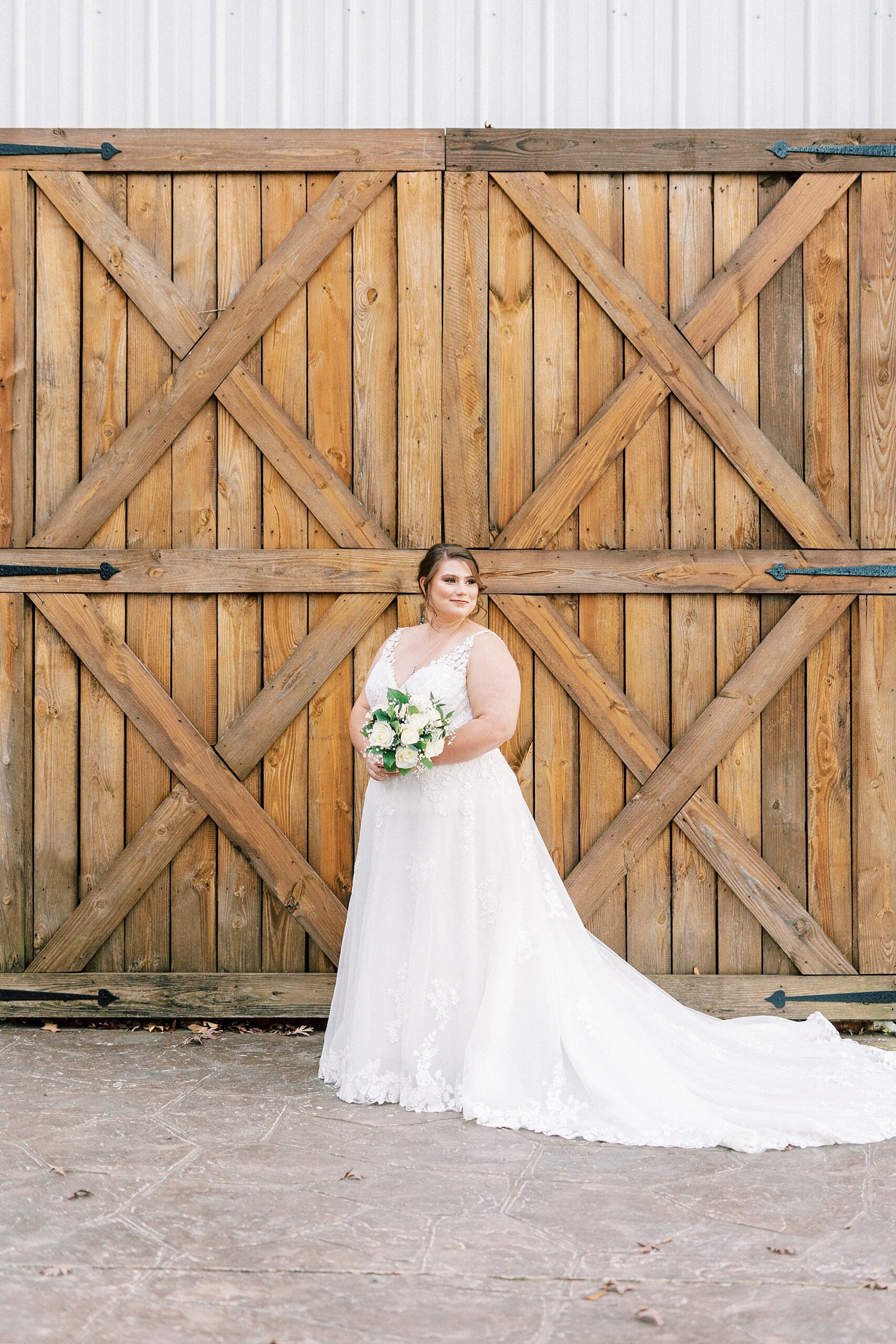 bride poses in front wooden barn doors and looks over her shoulder 