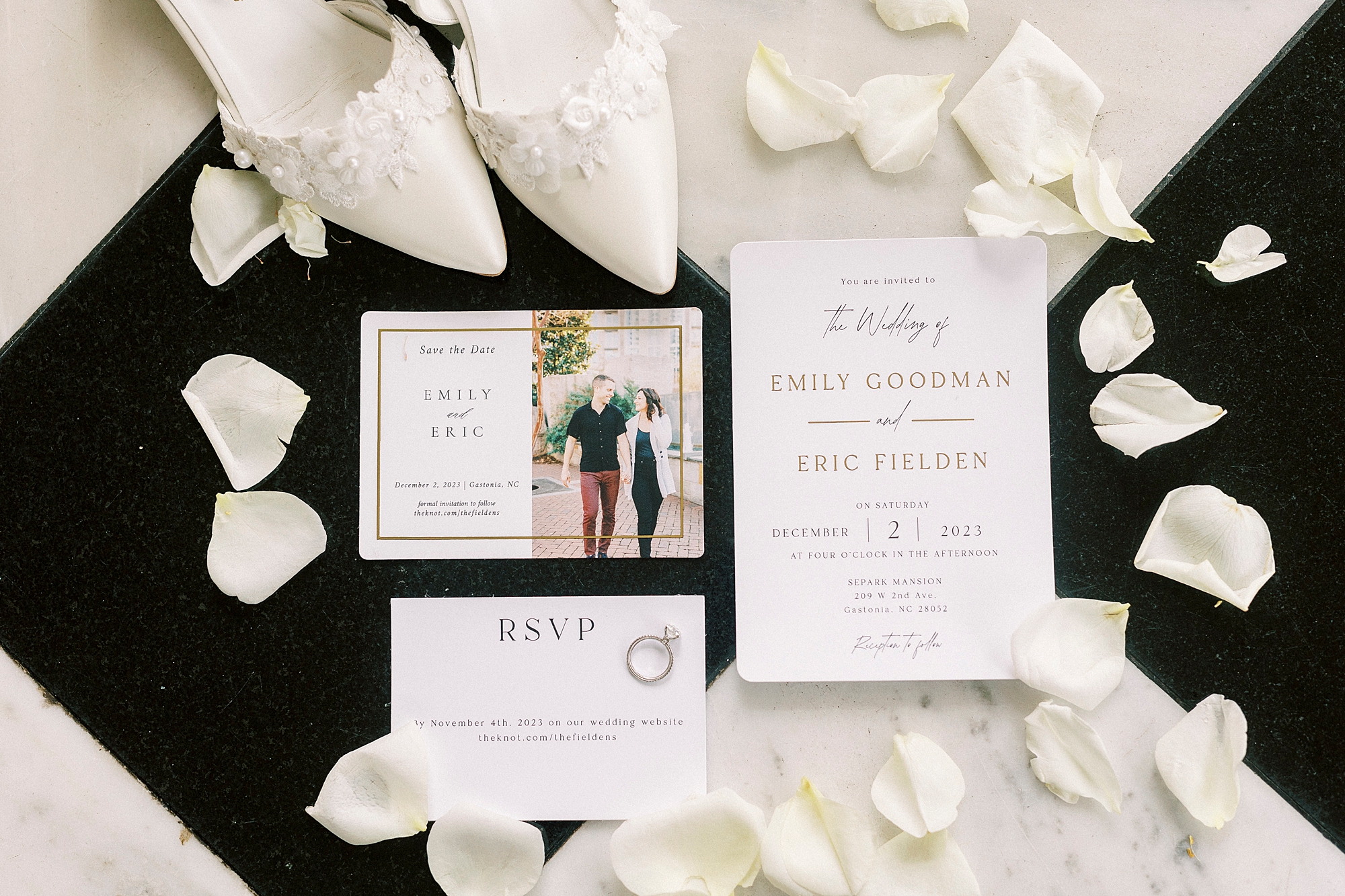 bride's ivory shoes and white flower petals on black and white floor around invitation suite 