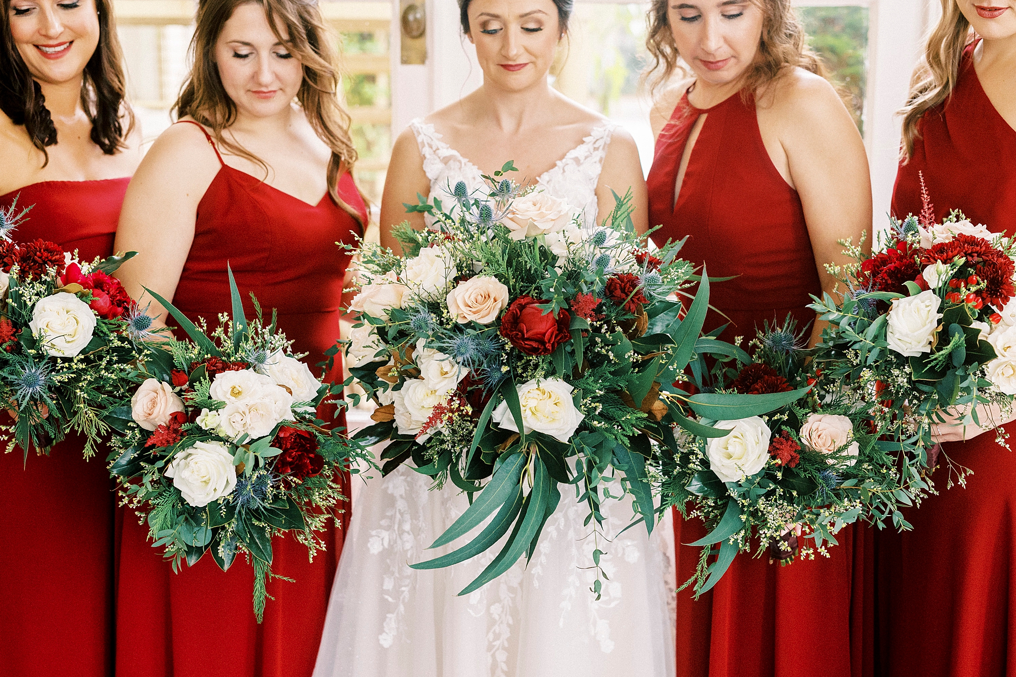 bride and bridesmaids in red gowns hold bouquets of white and red flowers for classic winter wedding at Separk Mansion