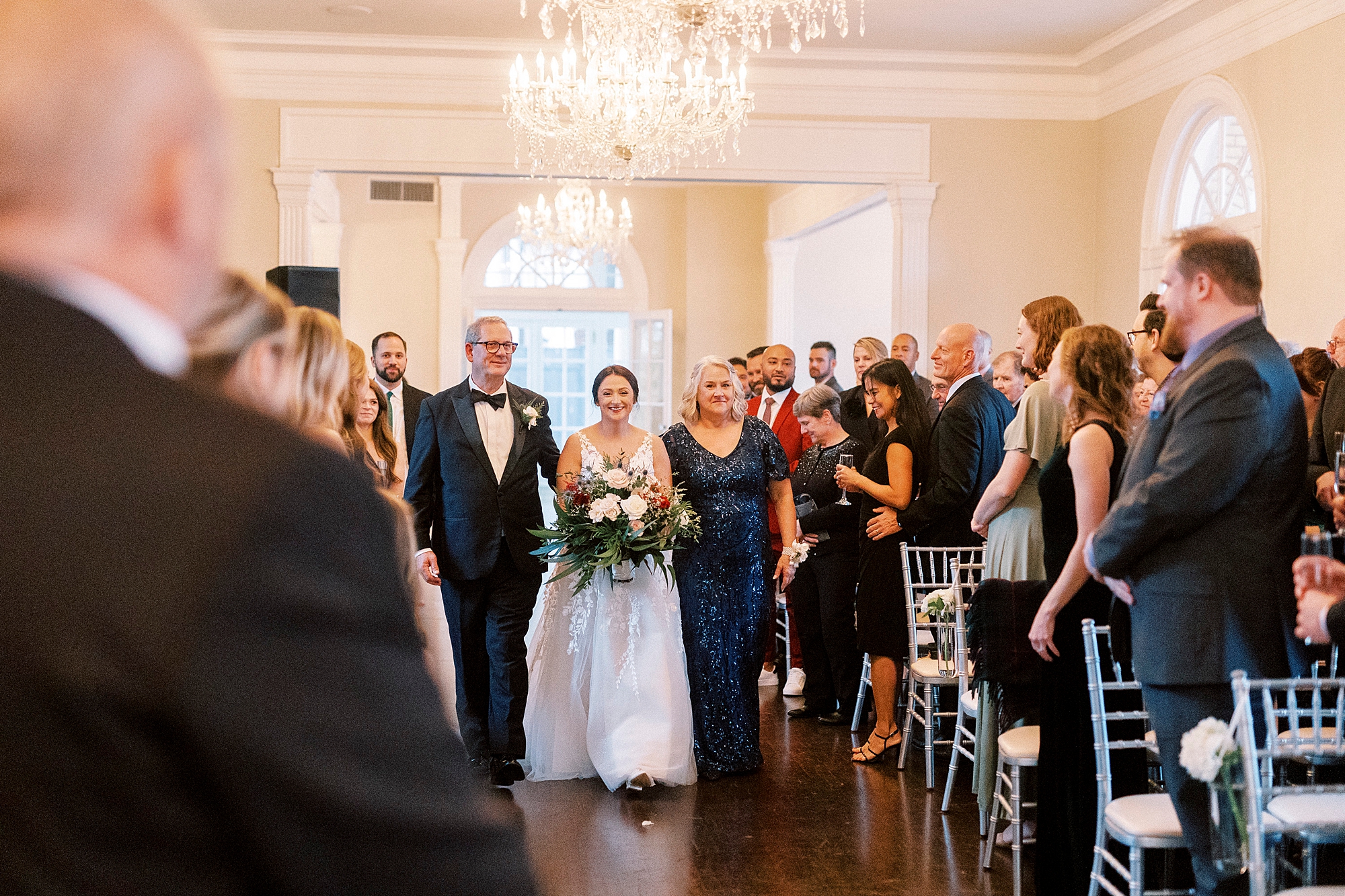 bride enters winter wedding ceremony at Separk Mansion with parents 