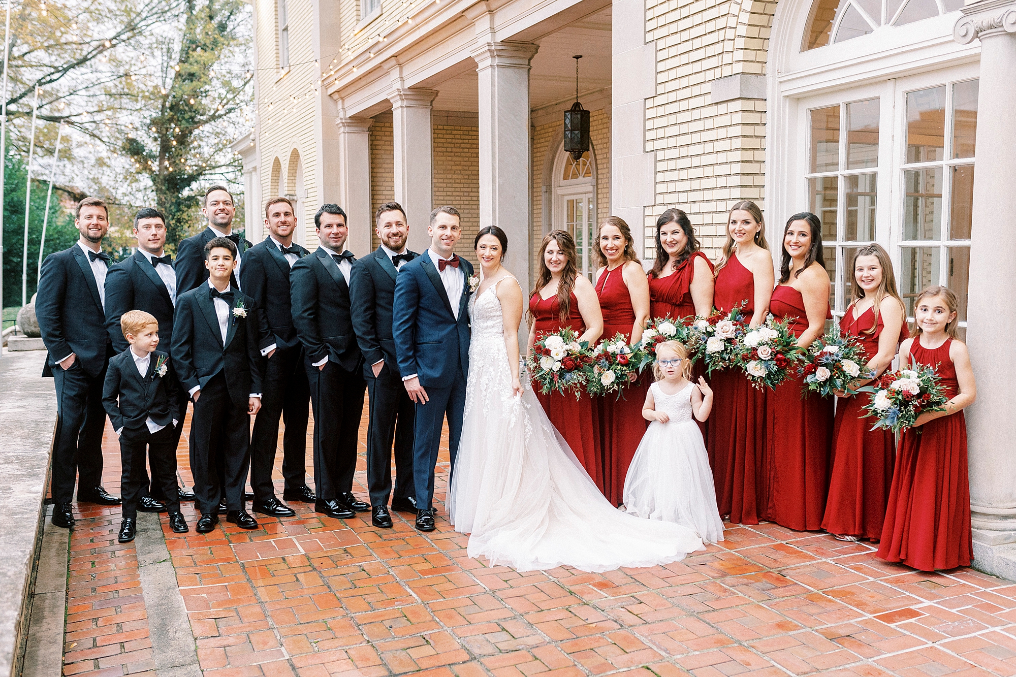 newlyweds pose with wedding party in navy suits and red gowns for classic winter wedding at Separk Mansion