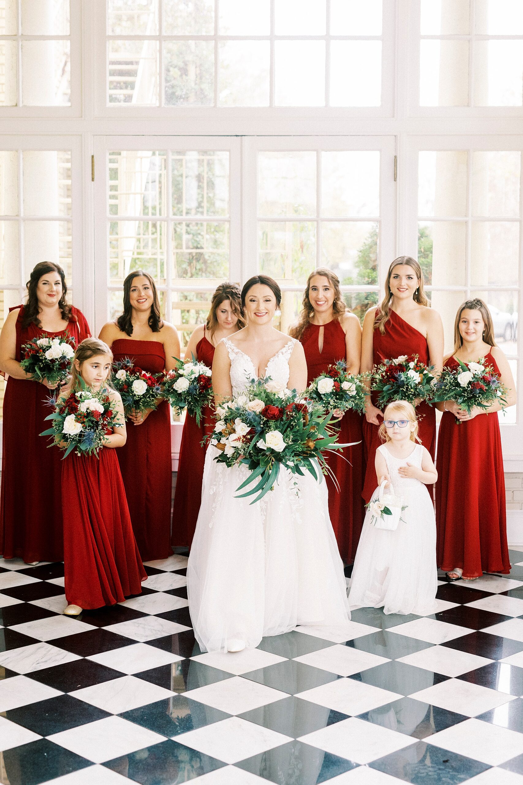 bride walks with bridesmaids in red gowns holding red and white bouquets 