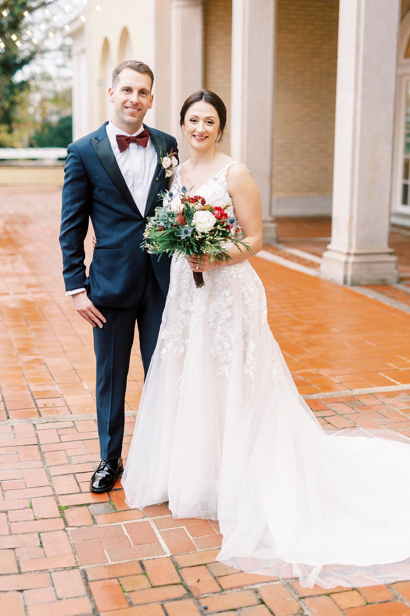 newlyweds stand together on rain covered brick patio