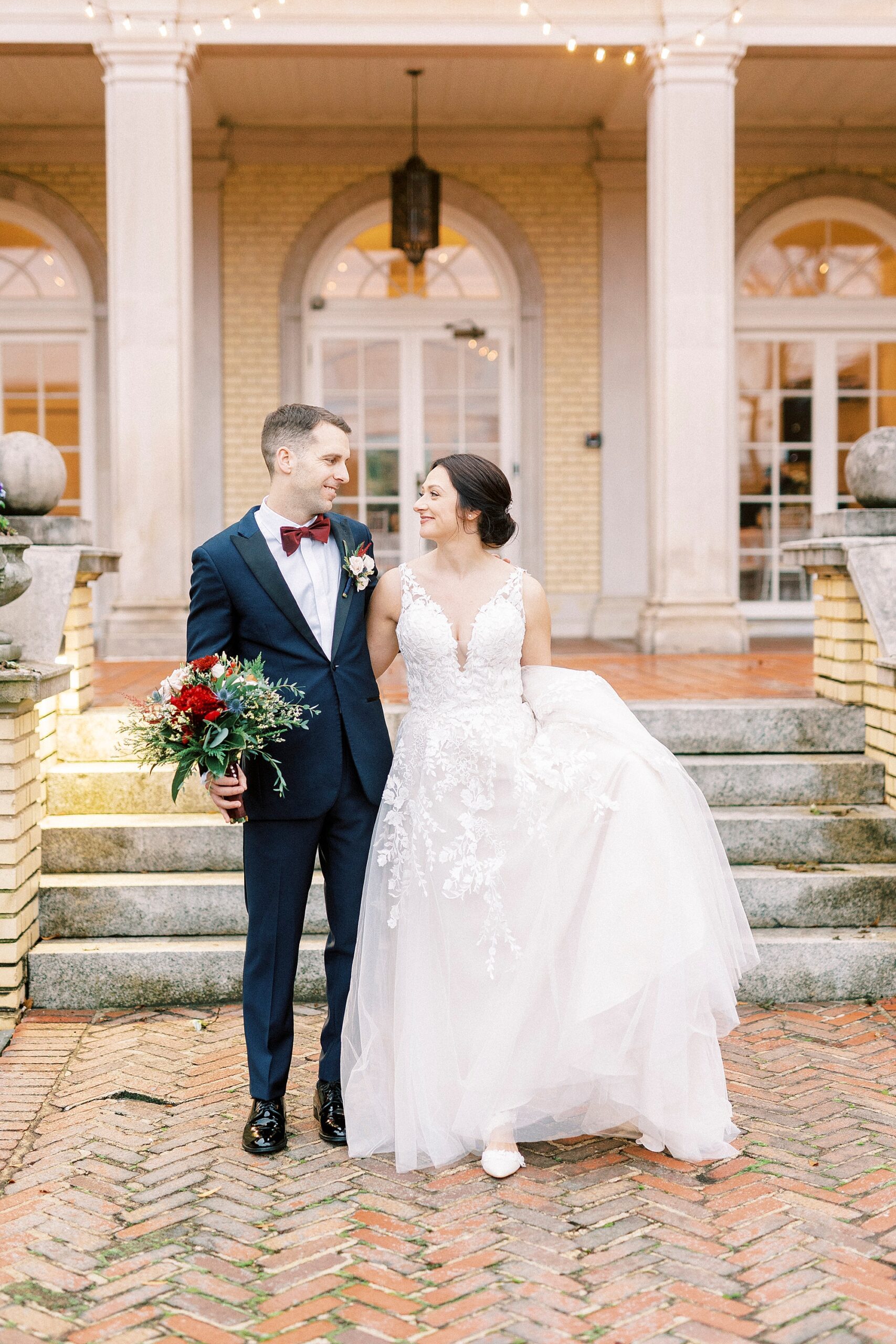 bride and groom stand in front of Separk Mansion while bride holds up wedding dress skirt 