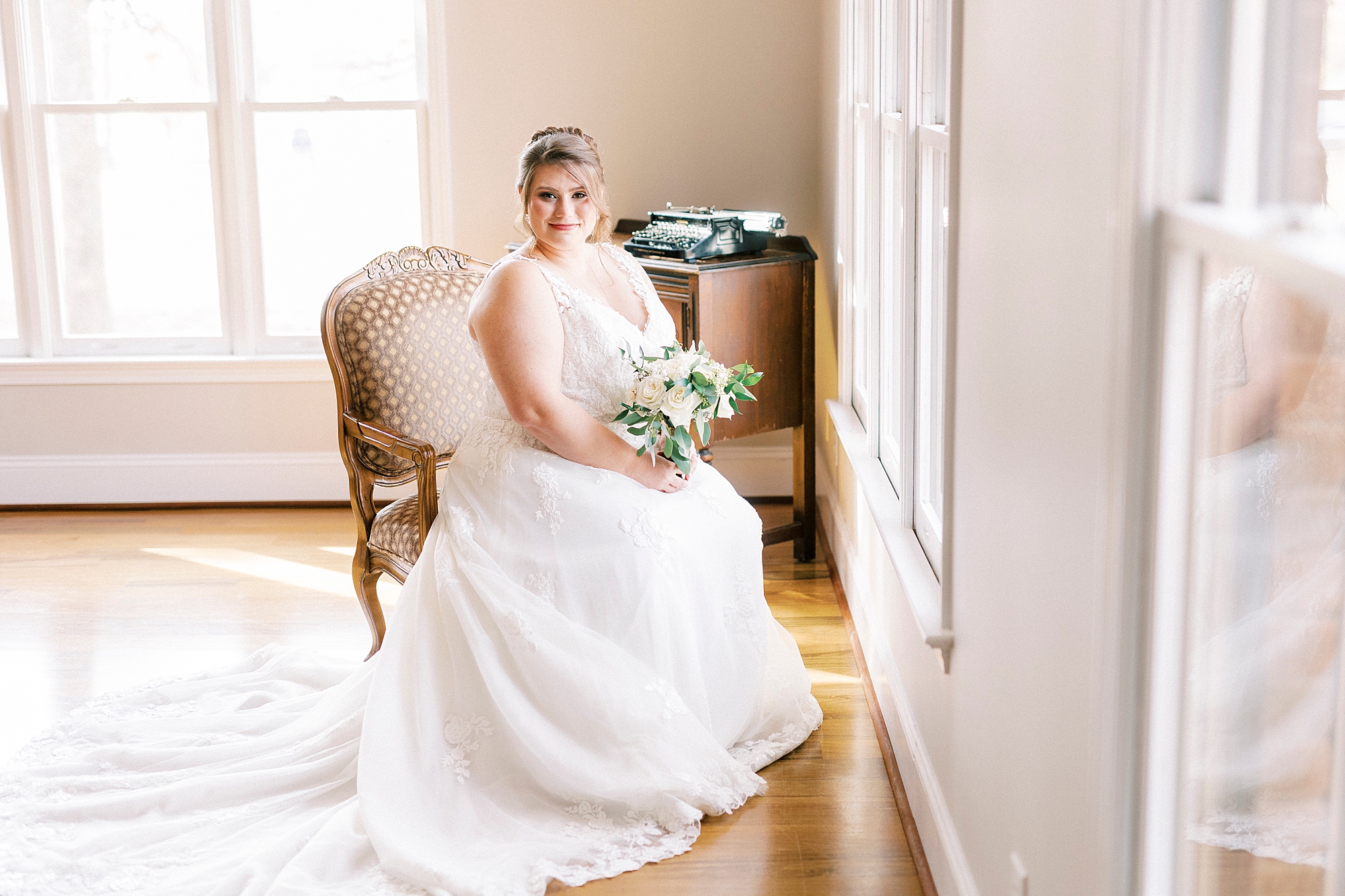 bride sits in chair holding bouquet facing window at the Farm at Brusharbor