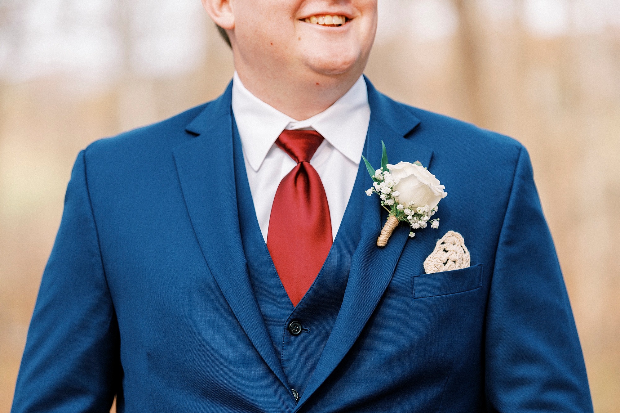 groom smiles in navy suit with red tie during fall wedding portraits 