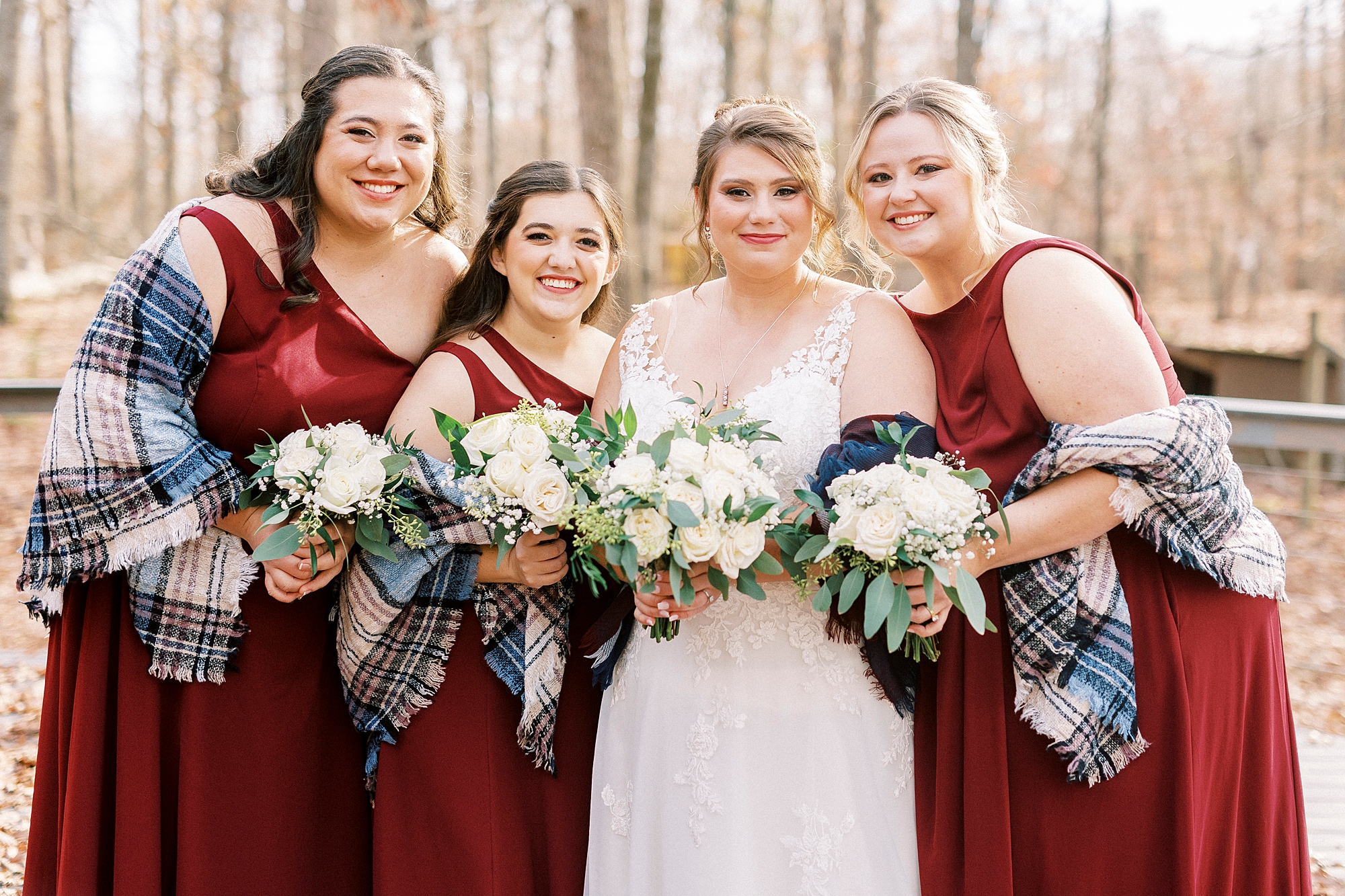 bride and bridesmaids in red gowns hug with blue flannel shawls 