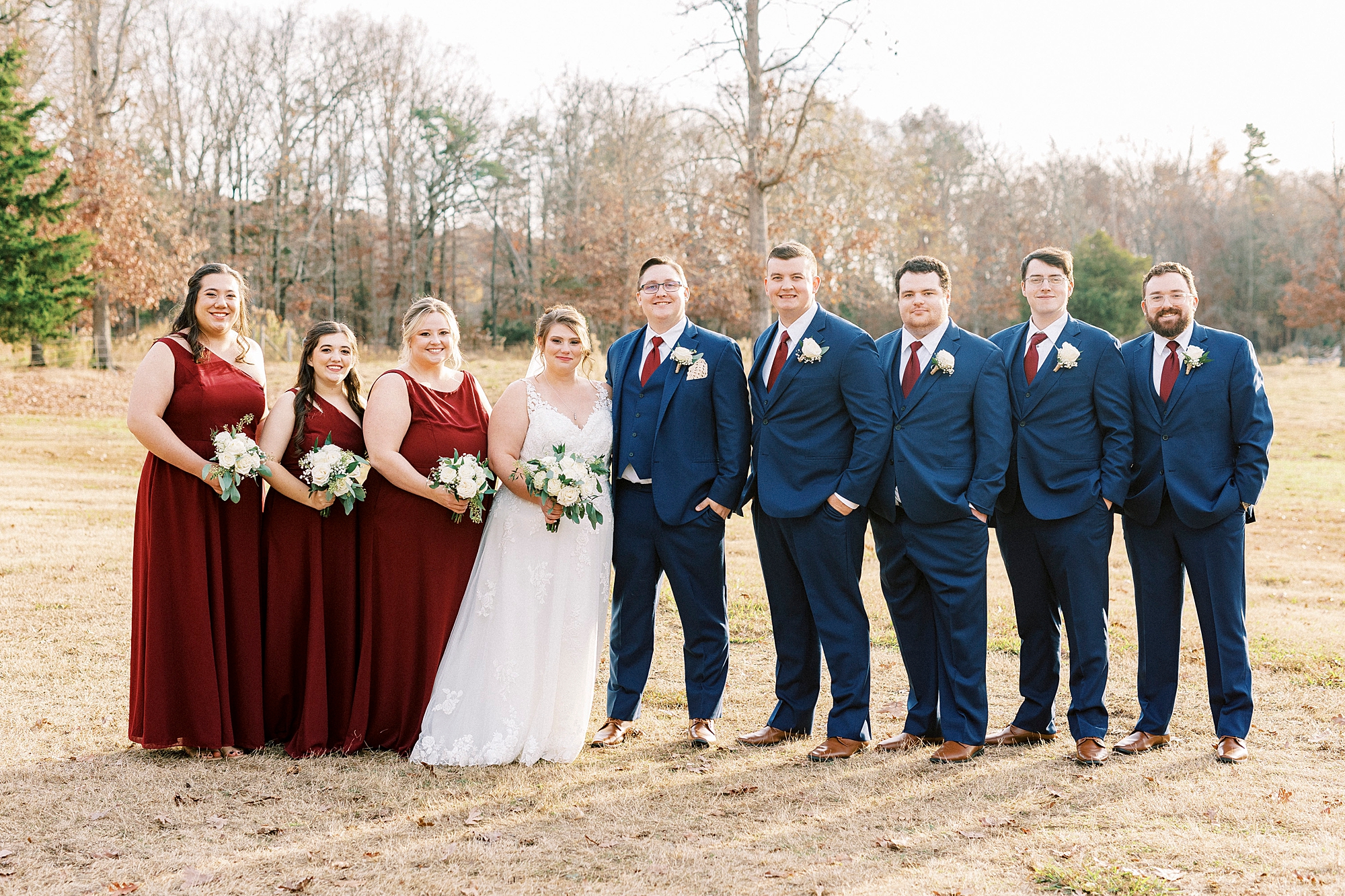 bride and groom pose with bridesmaids in red gowns and groomsmen in blue suits for fall wedding day