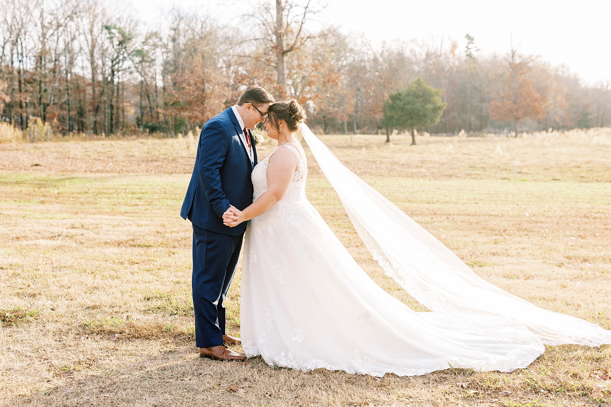 bride and groom stand together leaning into each other during fall wedding portraits 