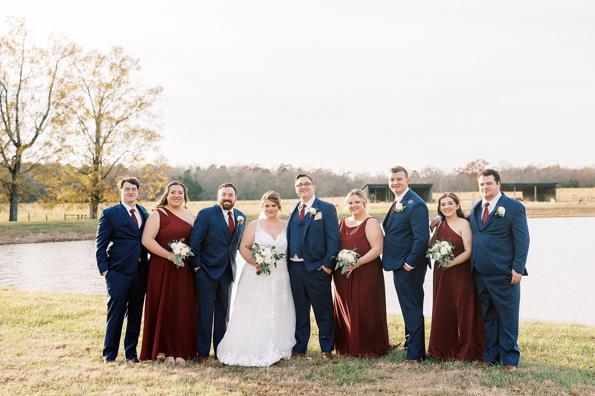 bride and groom stand with wedding party in burgundy gowns and navy suits 