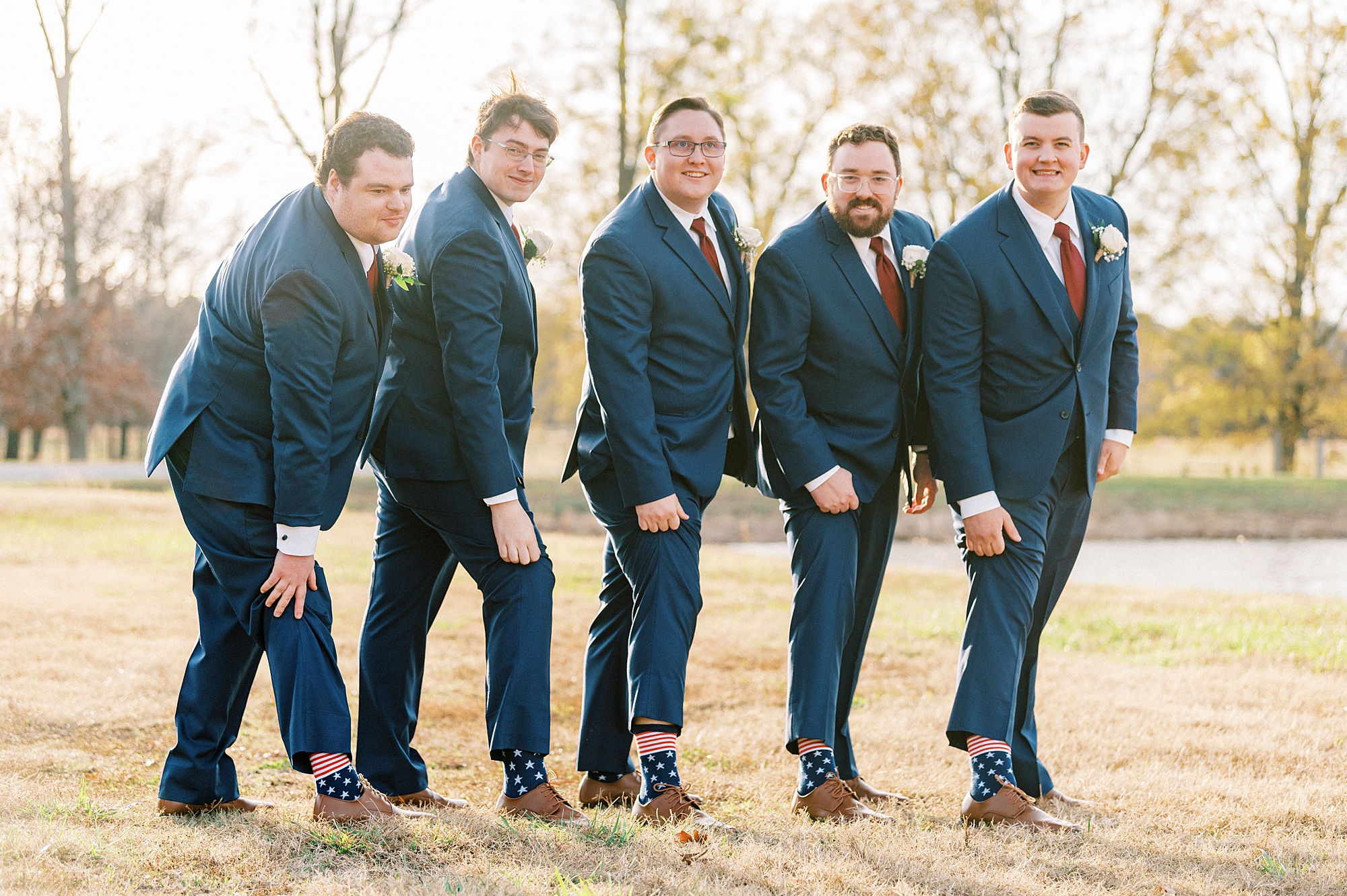 groom and groomsmen in navy suits lift up pants to show fun socks 
