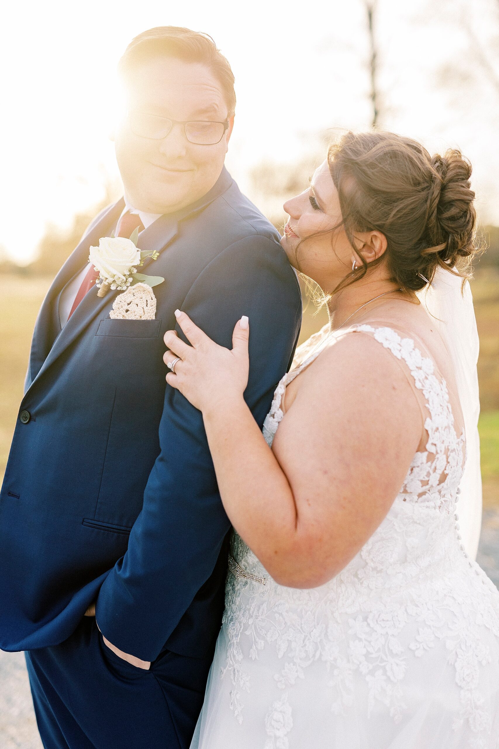 bride looks up at groom over his shoulder during fall wedding portraits at sunset 