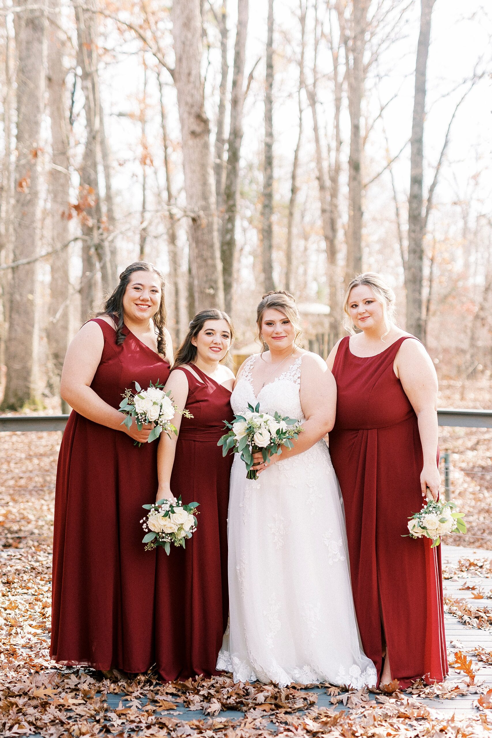 bride stands with three bridesmaids in red gowns for fall wedding at the Farm at Brusharbor