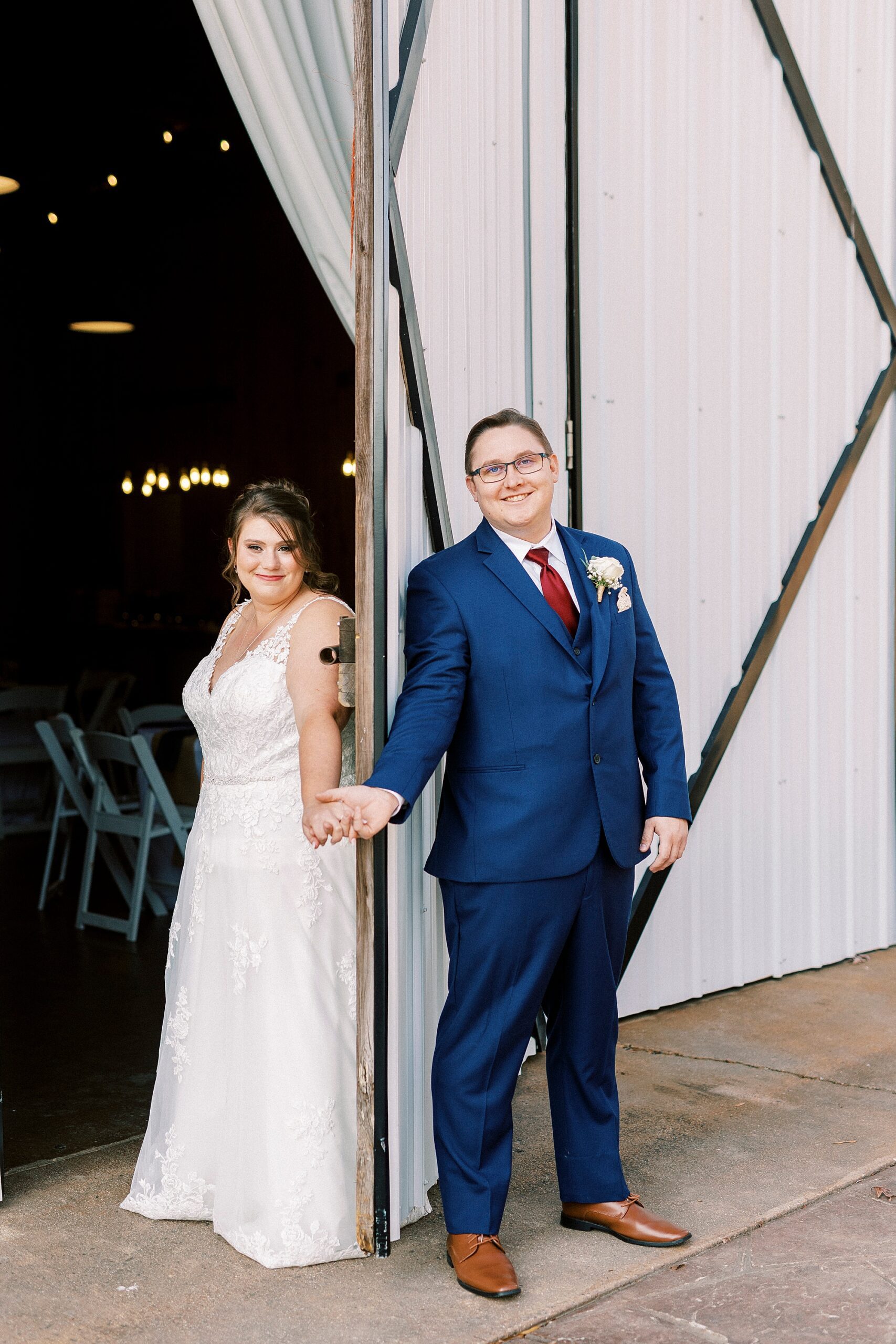 bride and groom hold hands around barn door for first touch at the Farm at Brusharbor
