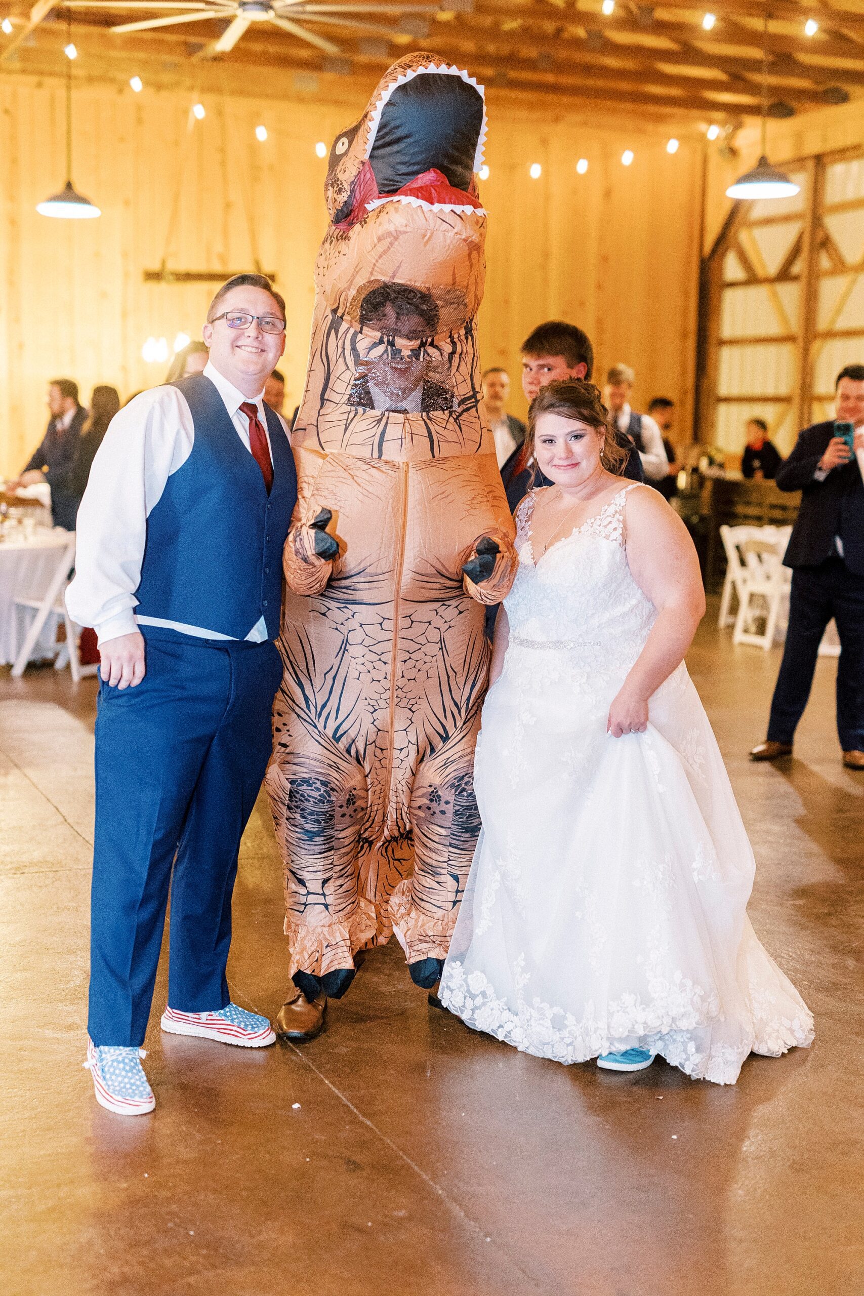 bride and groom pose with guest in t-rex costume during reception at the Farm at Brusharbor