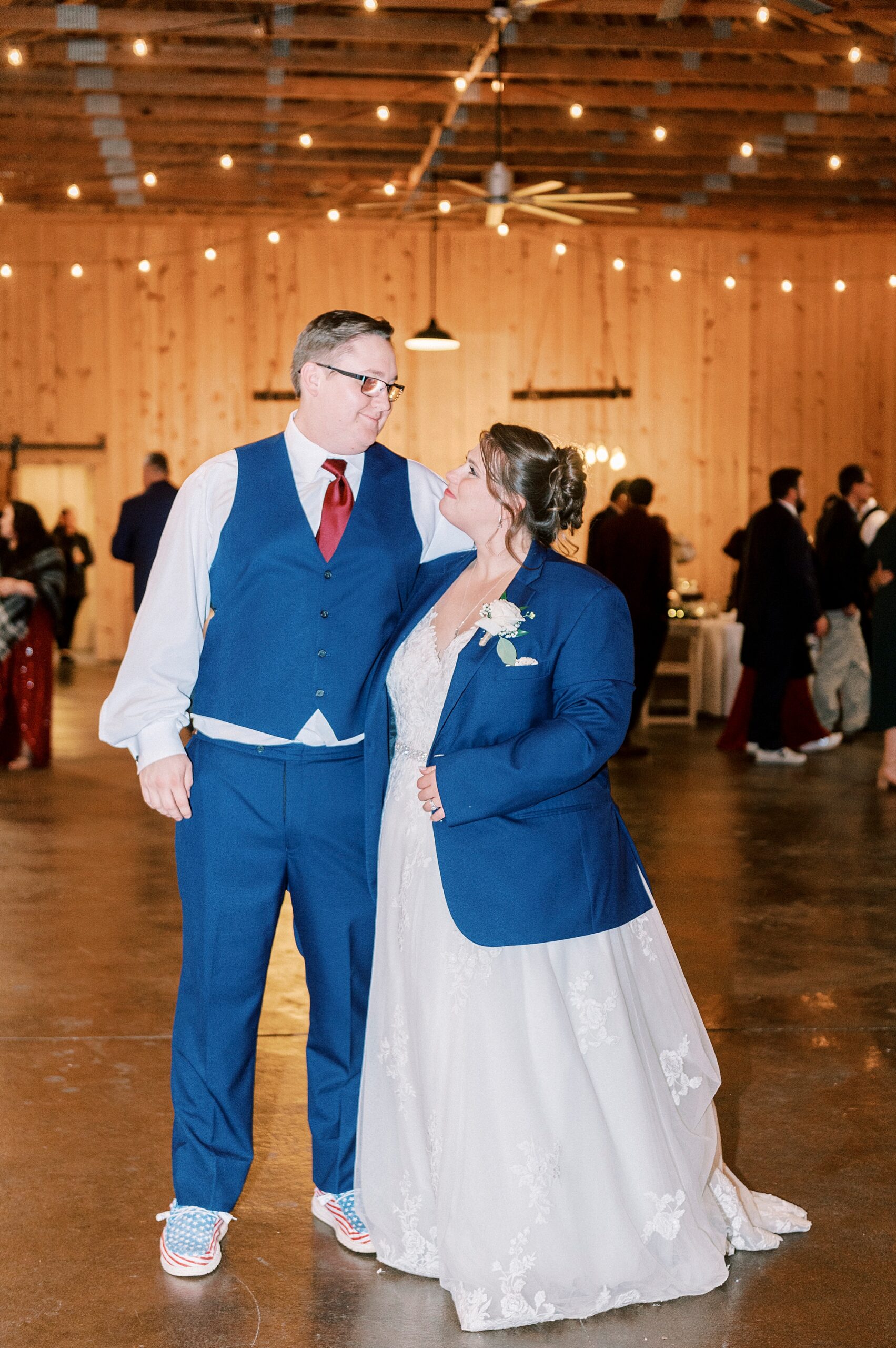 bride smiles up at groom wearing his suit jacket in barn at the Farm at Brusharbor