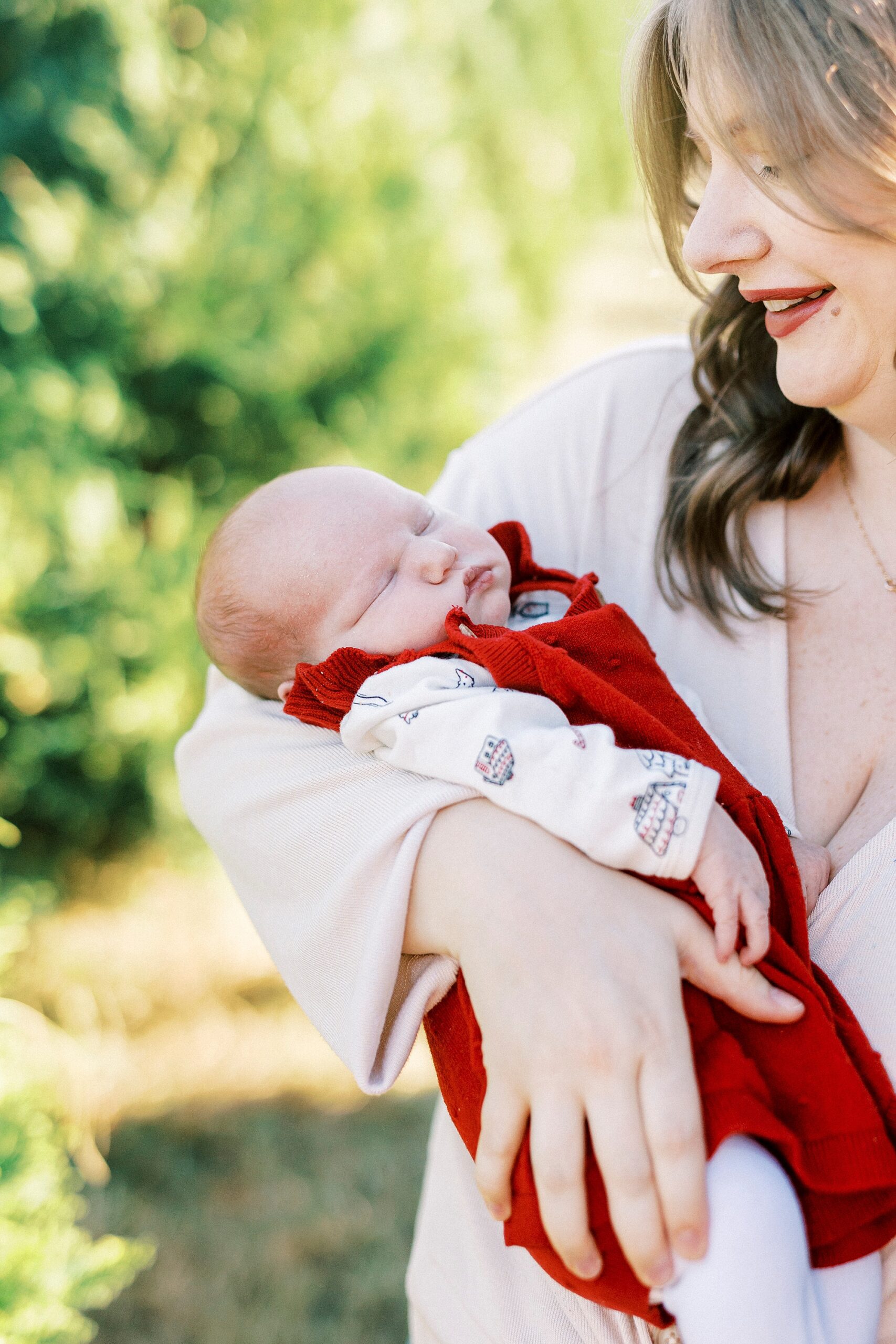 baby girl sleeps in red jumper in mom's arm during Penland Christmas Tree farm mini sessions 