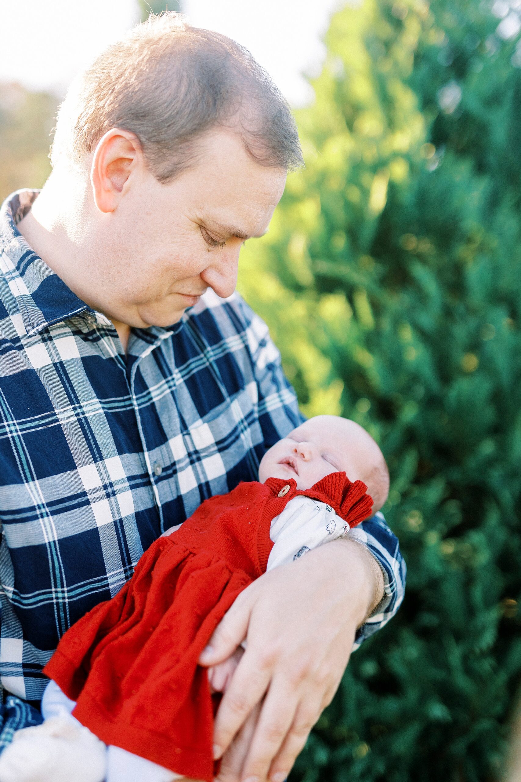 dad in blue plaid shirt looks down at baby girl in red dress