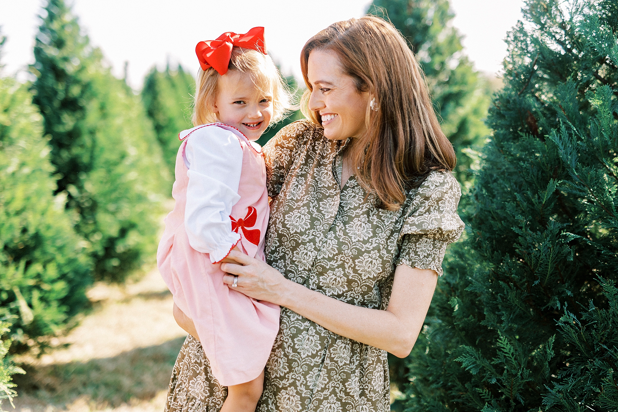 woman smiles with daughter on hip during mini sessions at Penland Christmas Tree Farm