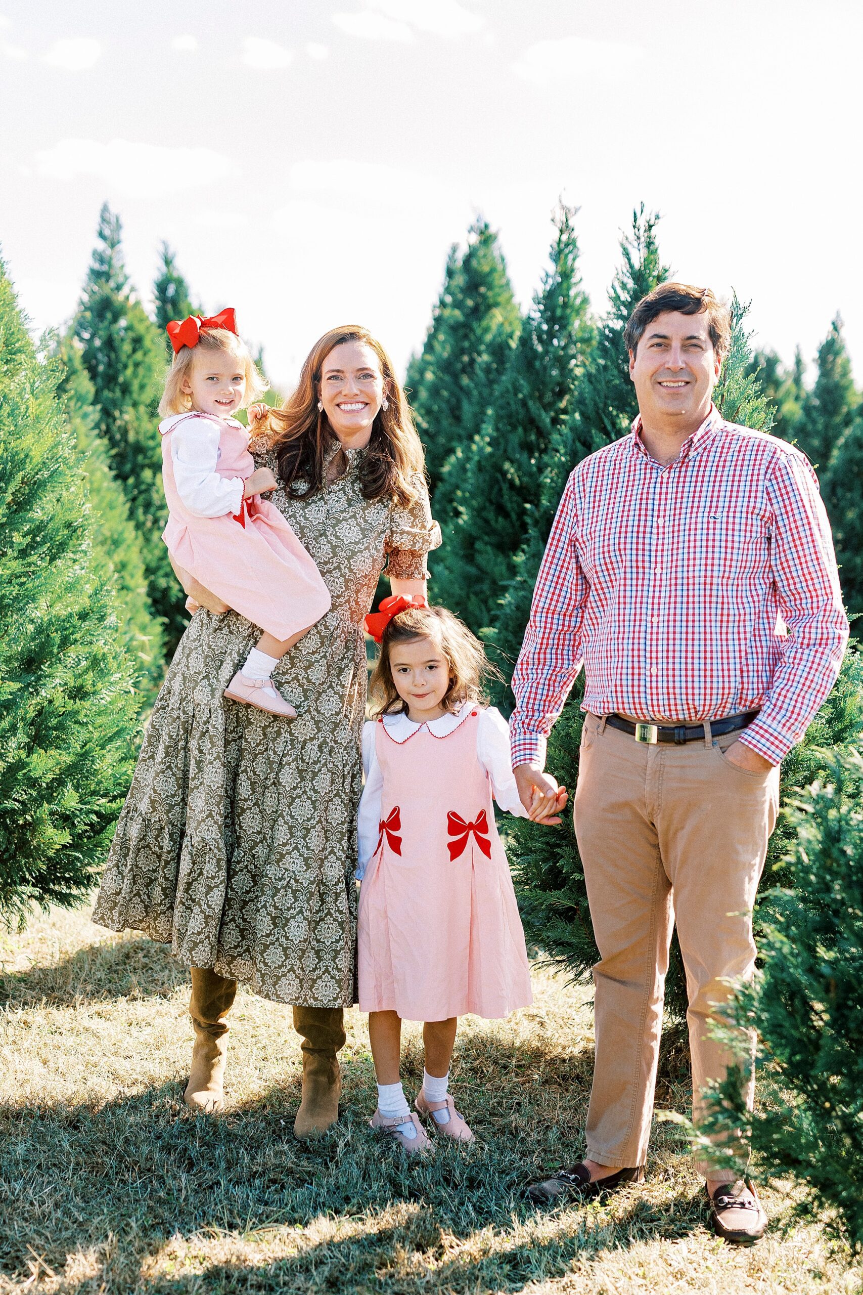 parents smile with two daughters between Christmas trees 
